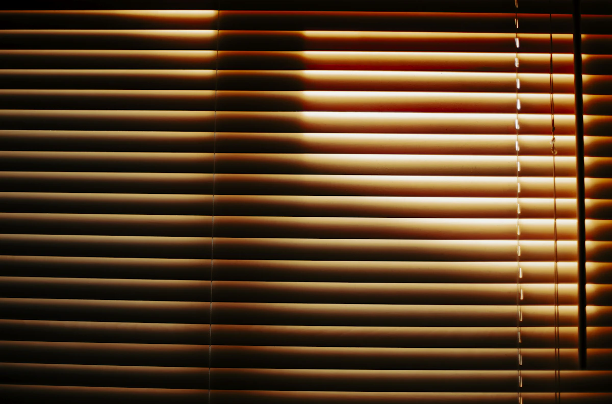 Primer plano de una cortina veneciana con la luz entrando entre las láminas
