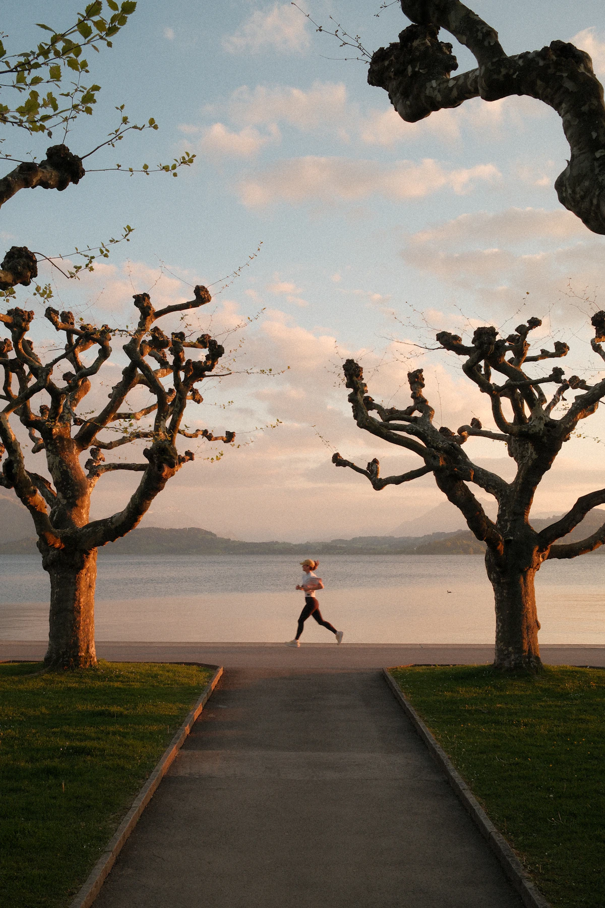 A woman jogging beside a calm lake at sunrise