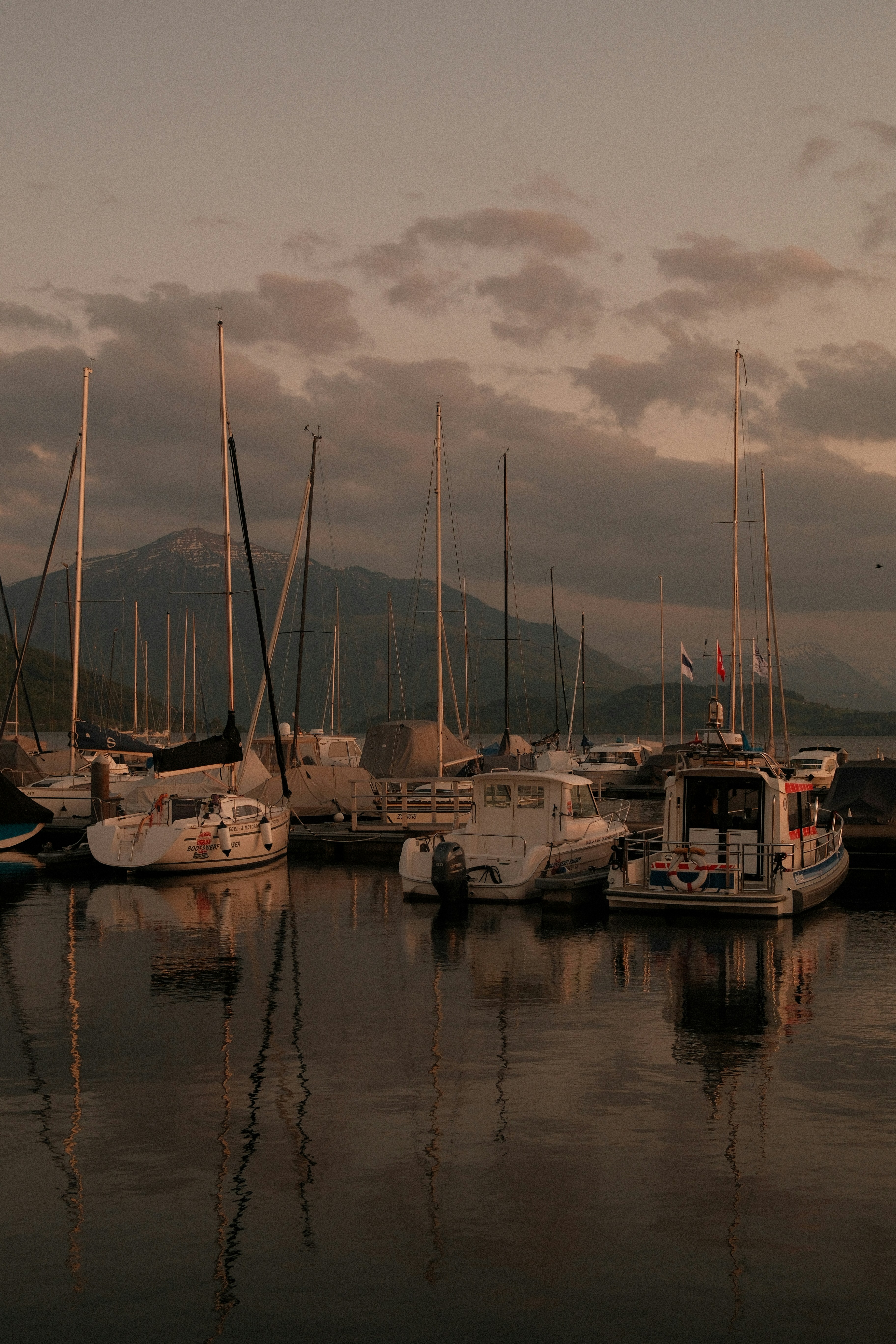 Perahu layar dan perahu motor berlabuh di pelabuhan saat senja.