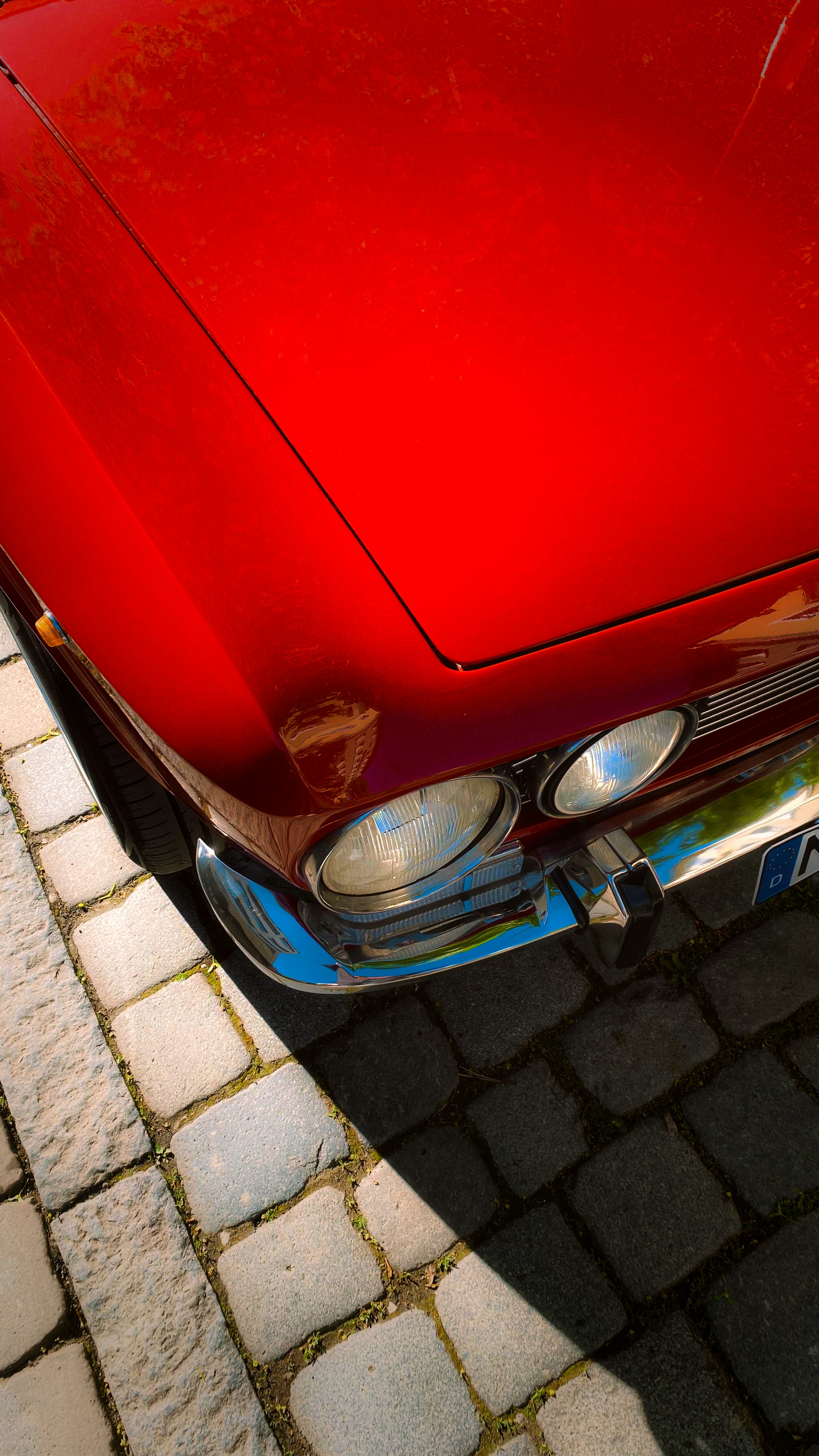 Primo piano di una griglia e fari di un'auto vintage rossa lucida.