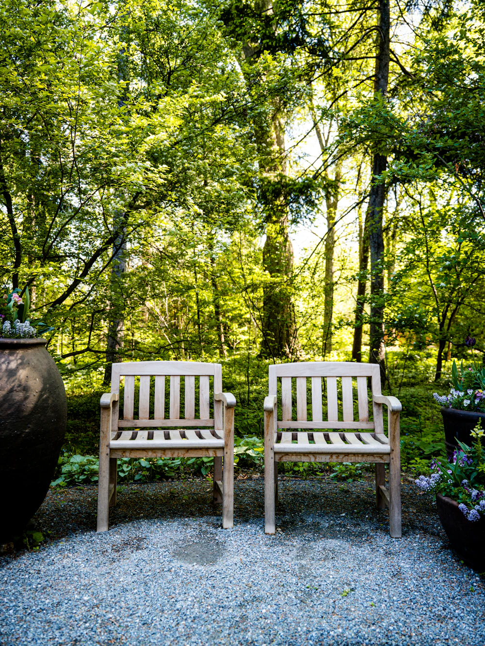 Two wooden garden chairs side by side among green trees
