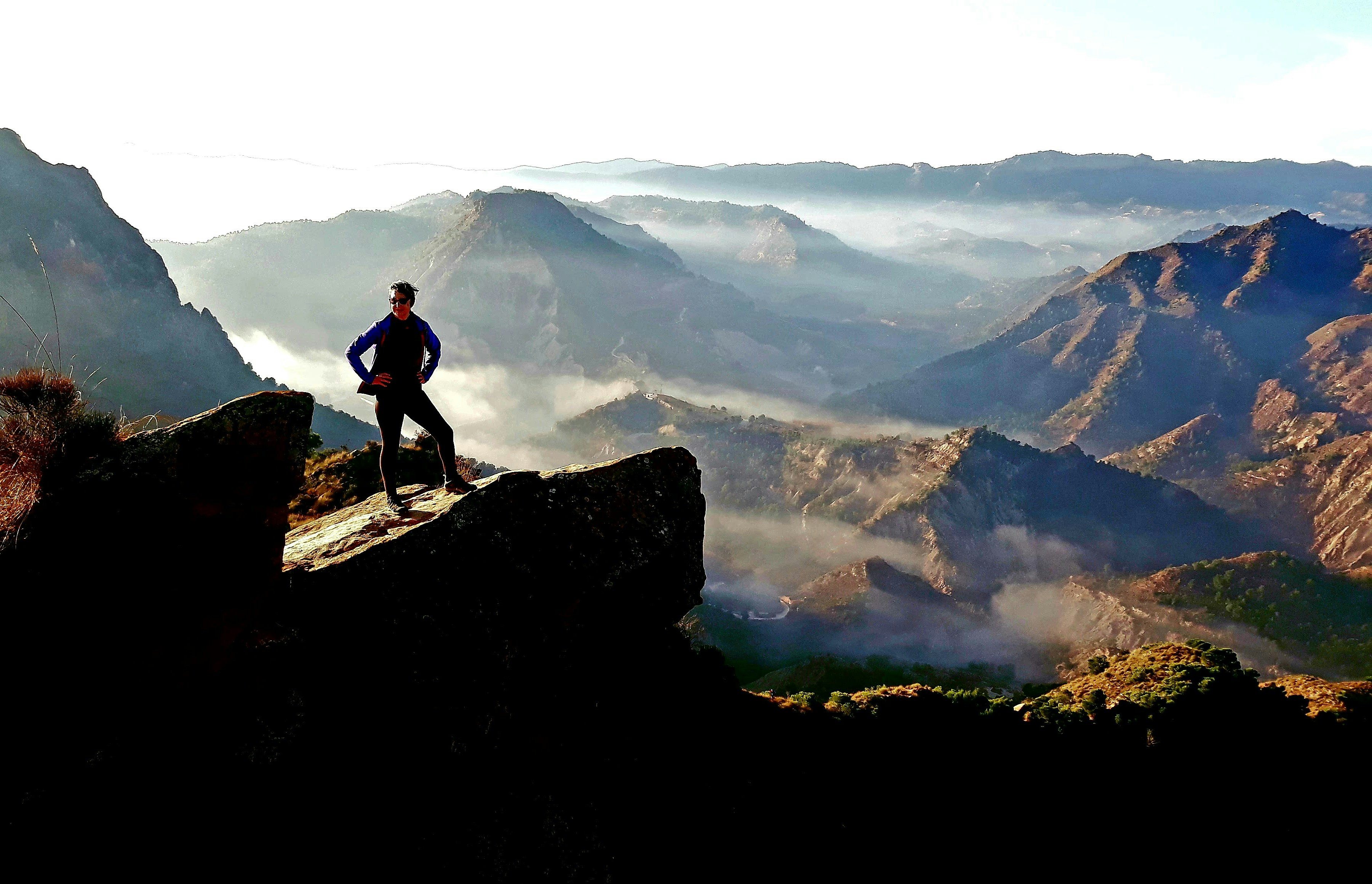 Man standing on rocky outcrop overlooking misty mountains