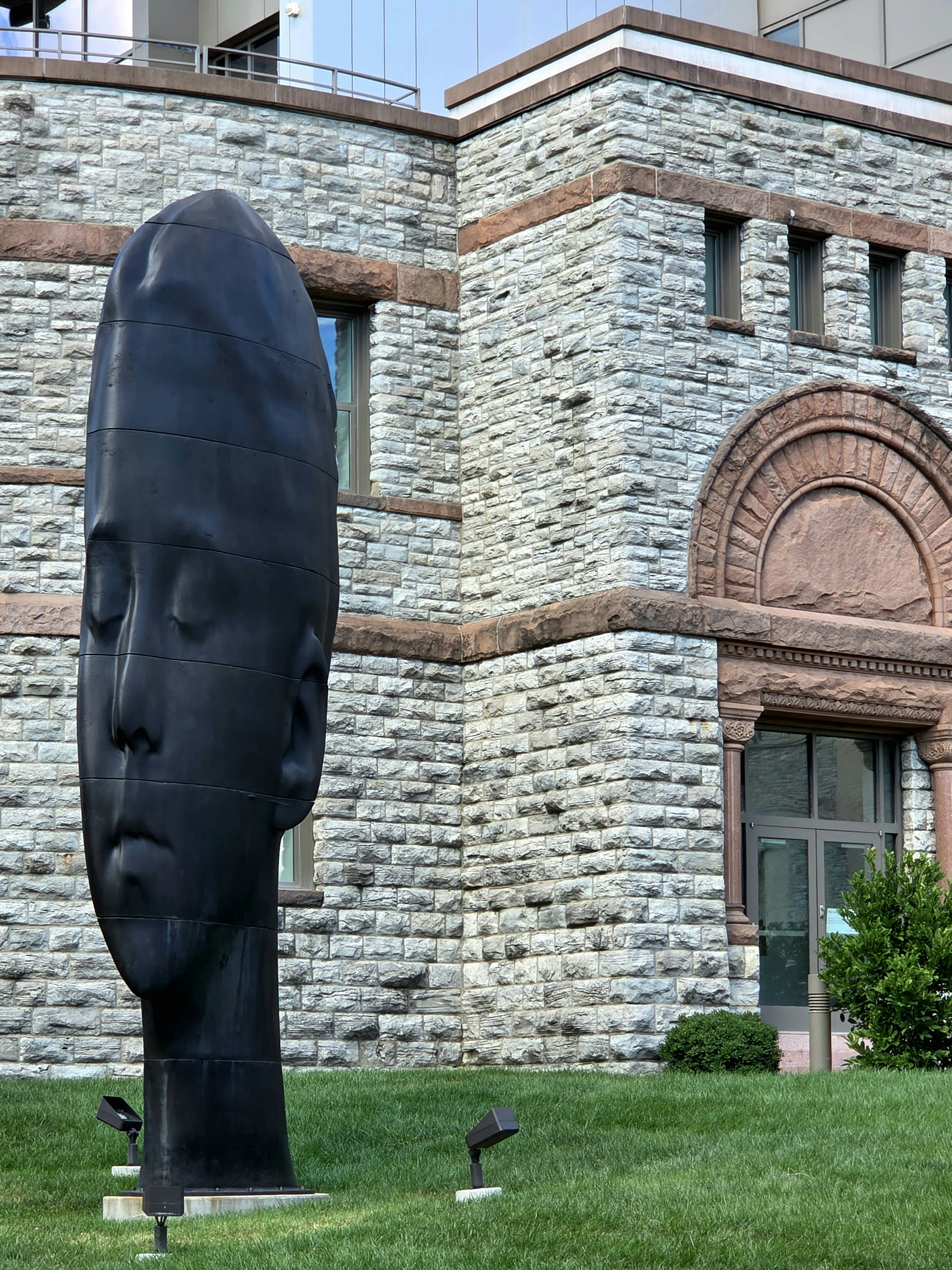Large dark head sculpture in front of stone building