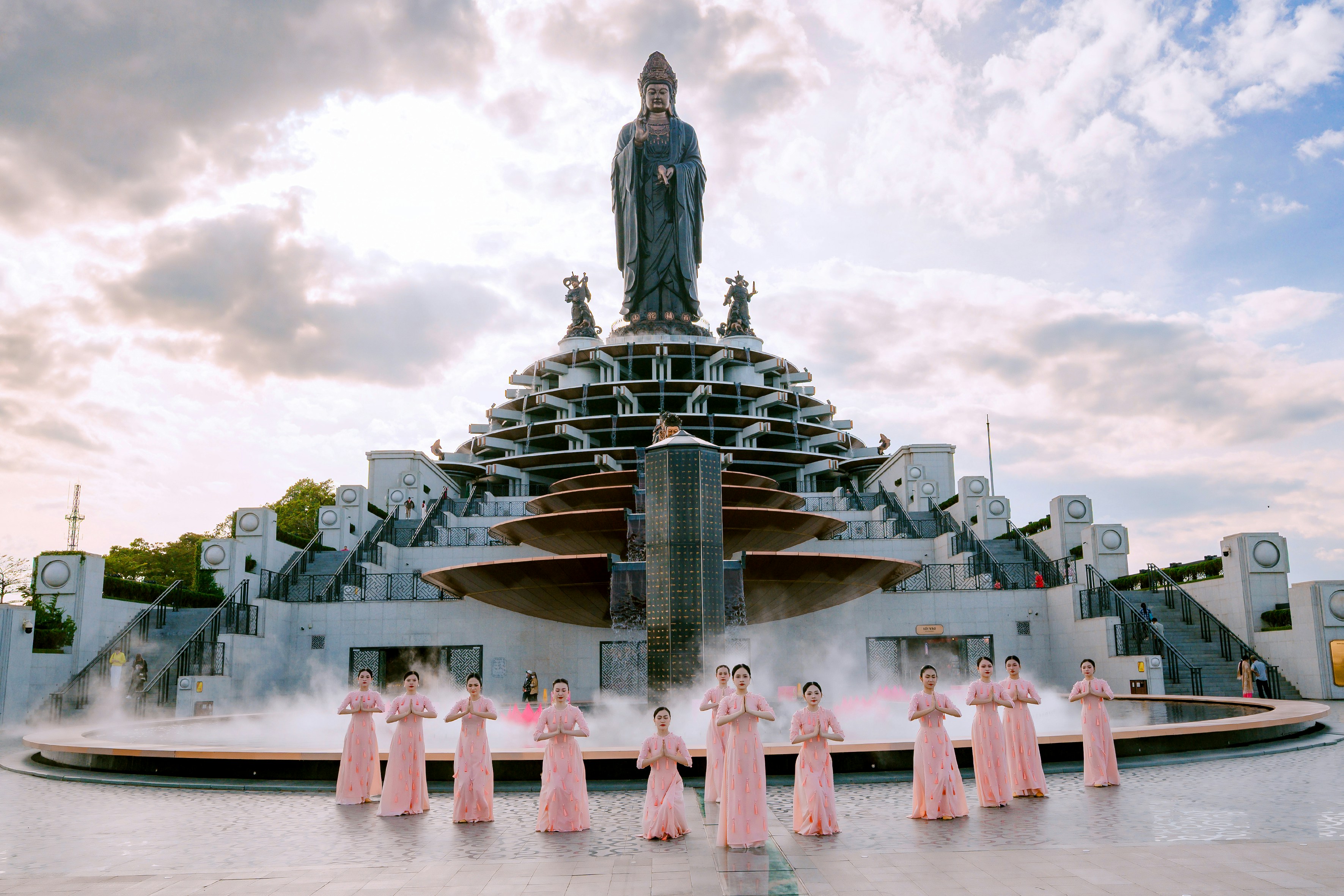 Grande estátua no topo de uma estrutura em degraus com pessoas vestidas de rosa