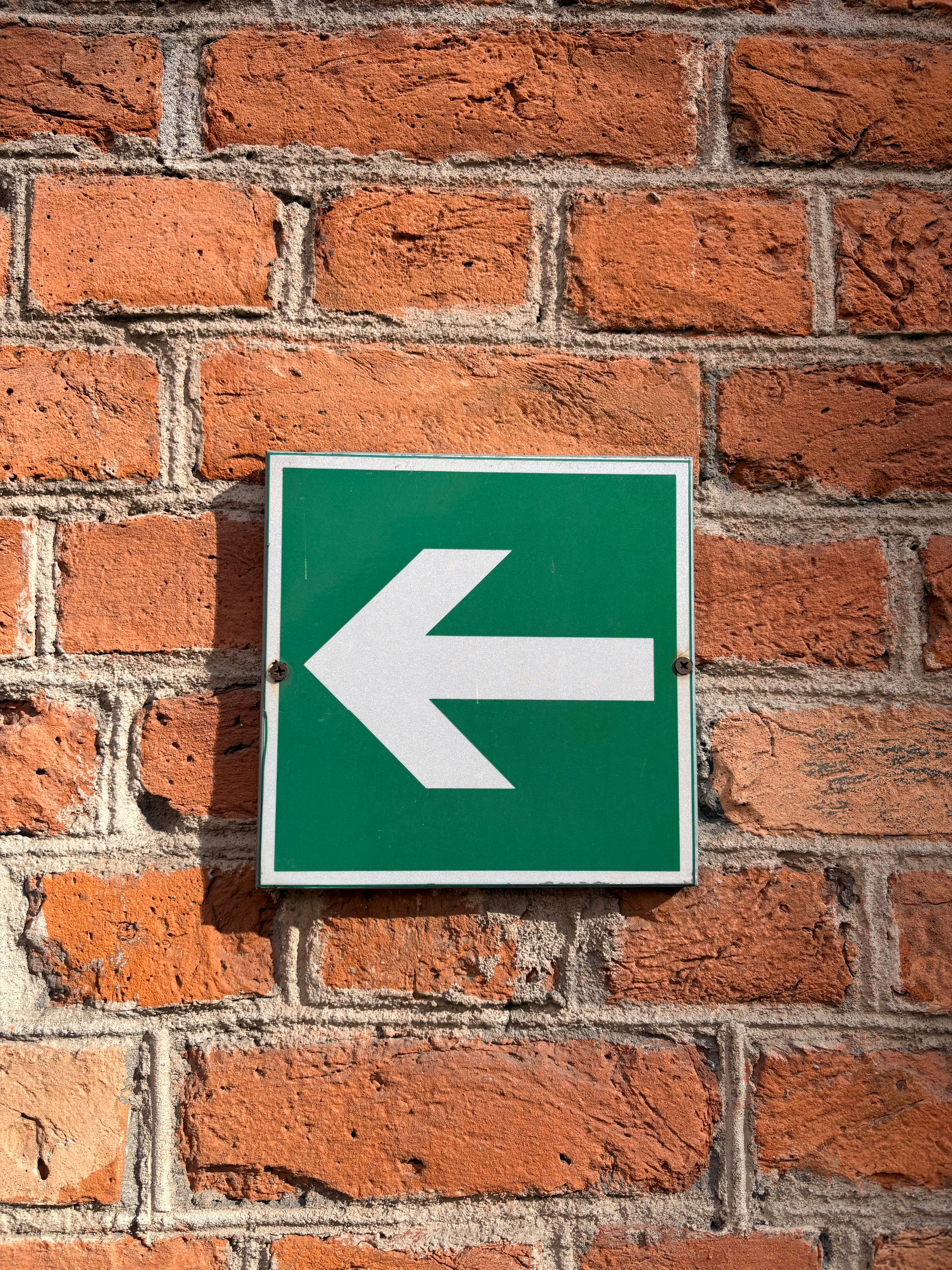 Panneau vert avec une flèche blanche pointant vers la gauche sur un mur de briques