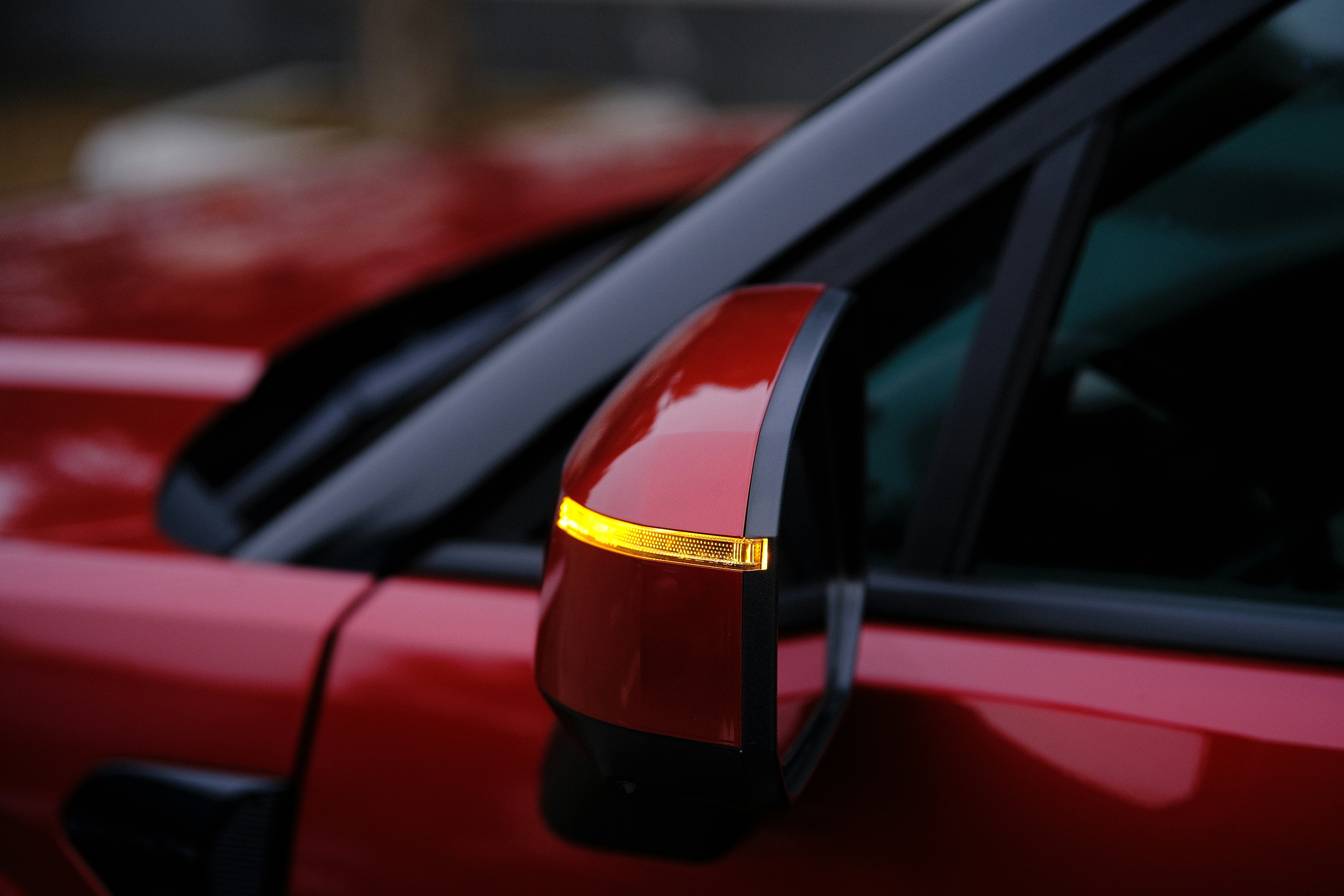 Close-up of a red car's side mirror with turn signal.