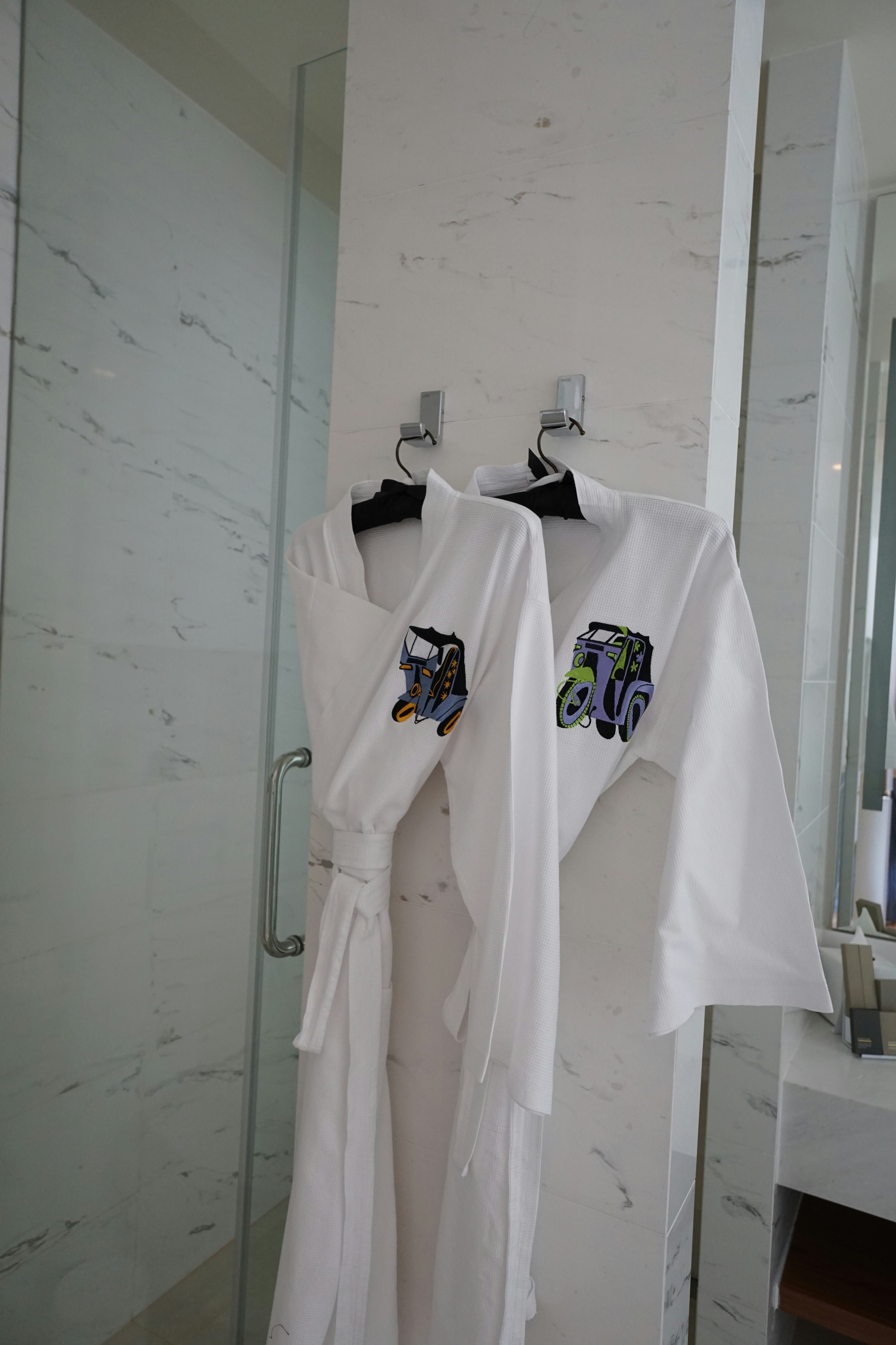 Two white robes hanging on hooks in a bathroom.