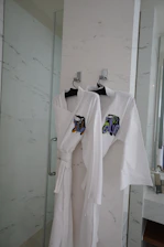 Two white robes hanging on hooks in a bathroom.