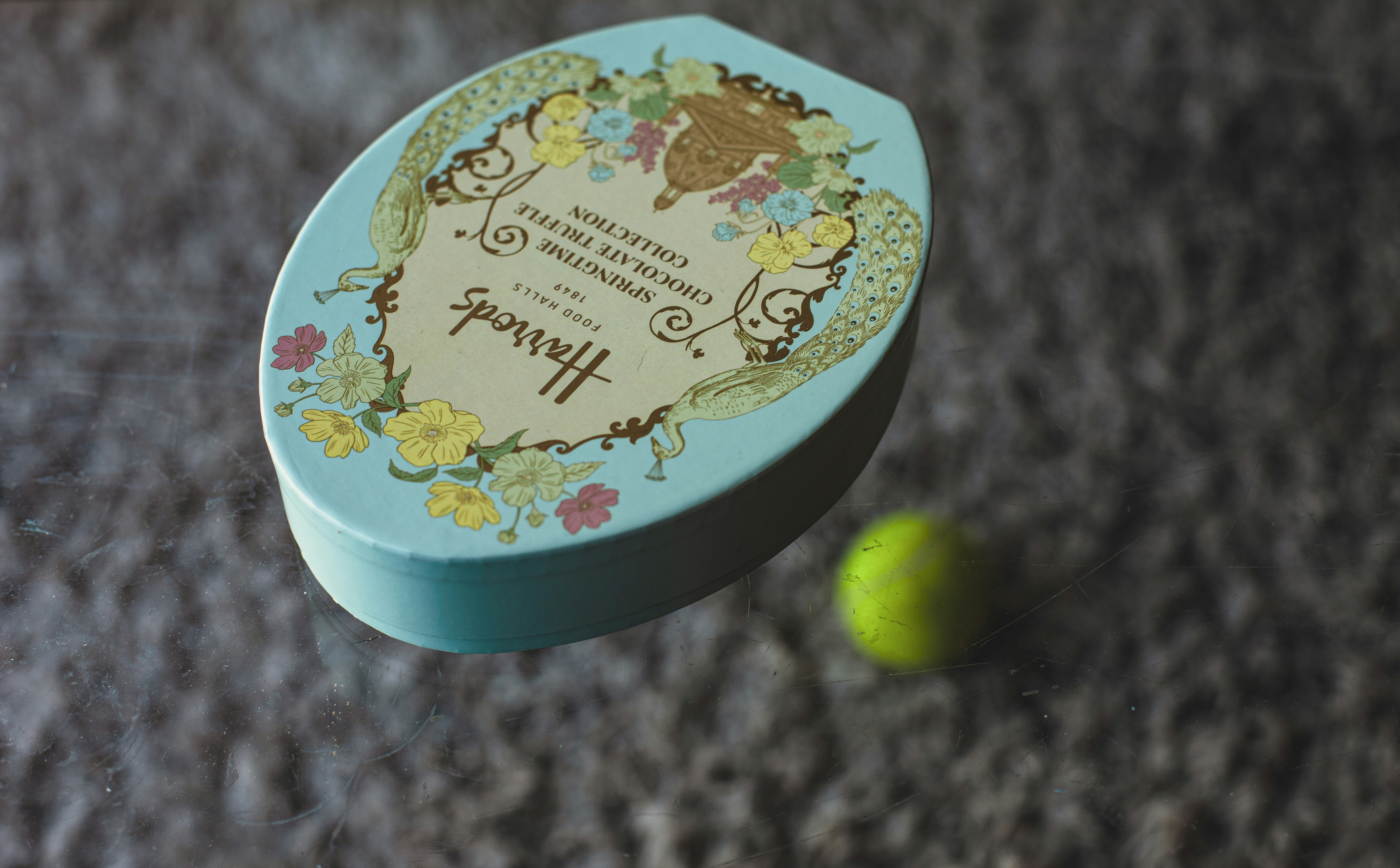 A teal oval tin box with floral designs and text.