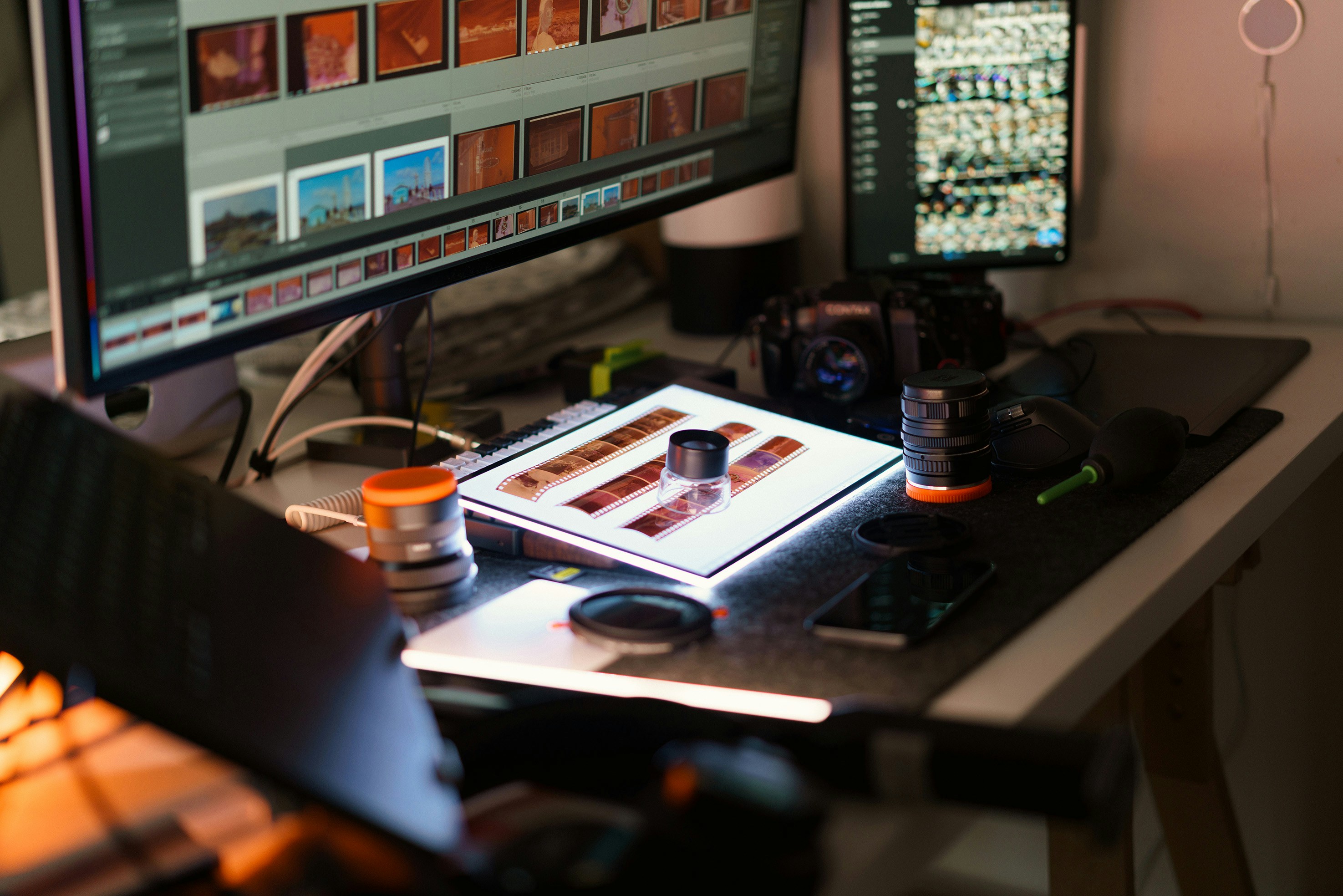 Meja dengan monitor komputer dan peralatan fotografi.