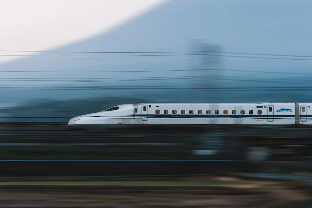 A white shinkansen train passing at speed with Mount Fuji behind it