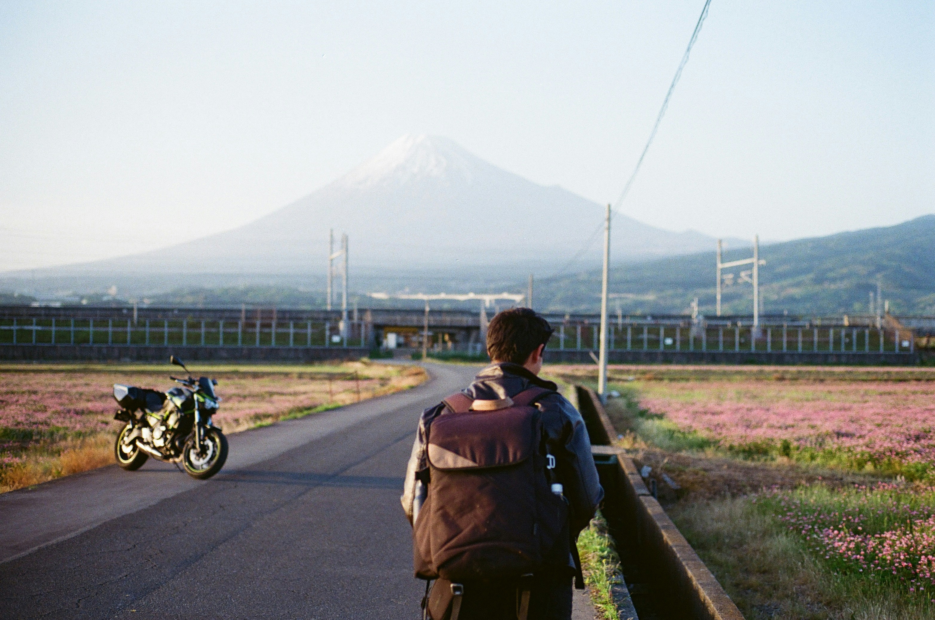 Man walks down road towards mount fuji with motorcycle.