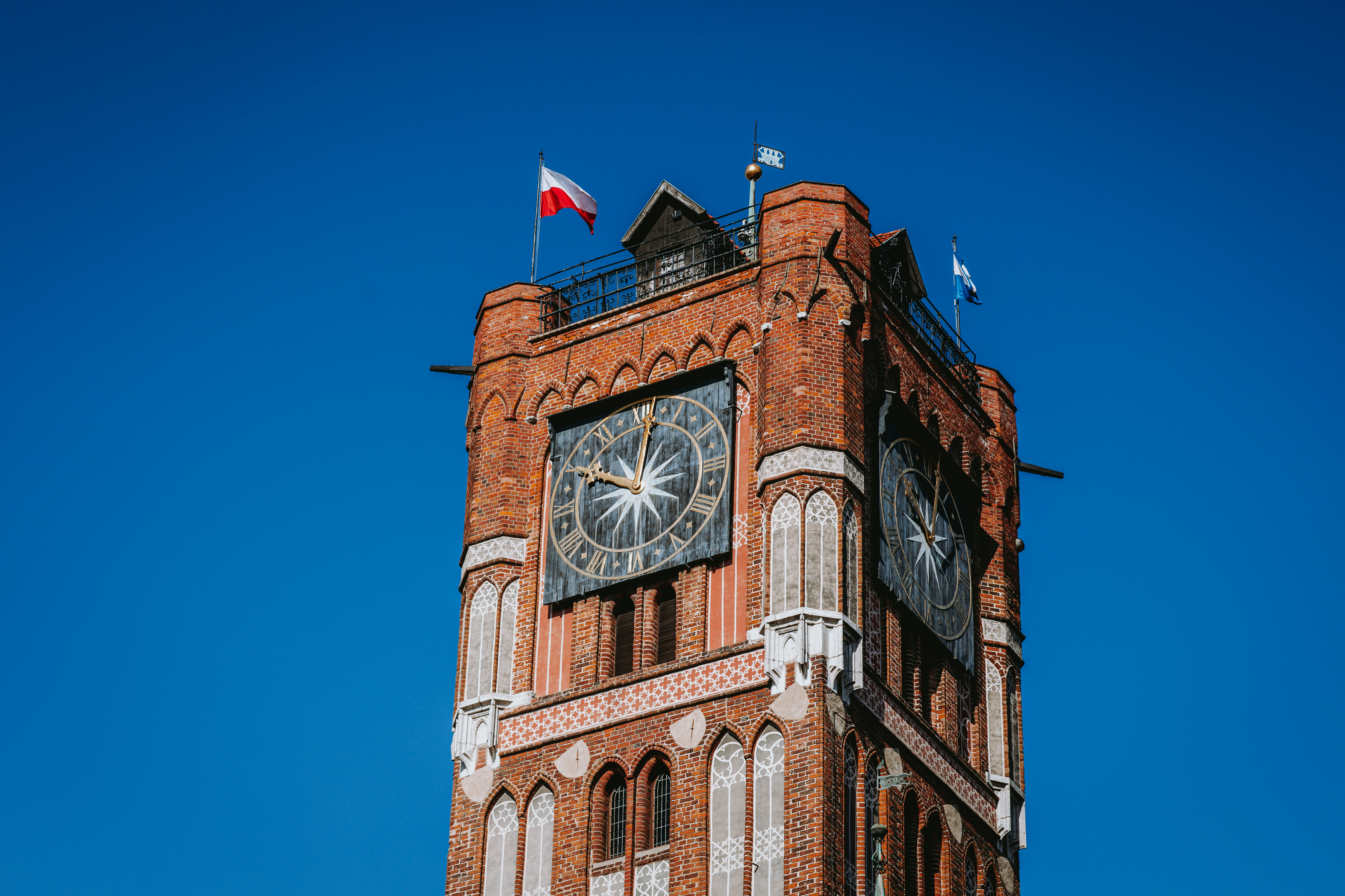 Brick clock tower with flags against blue sky
