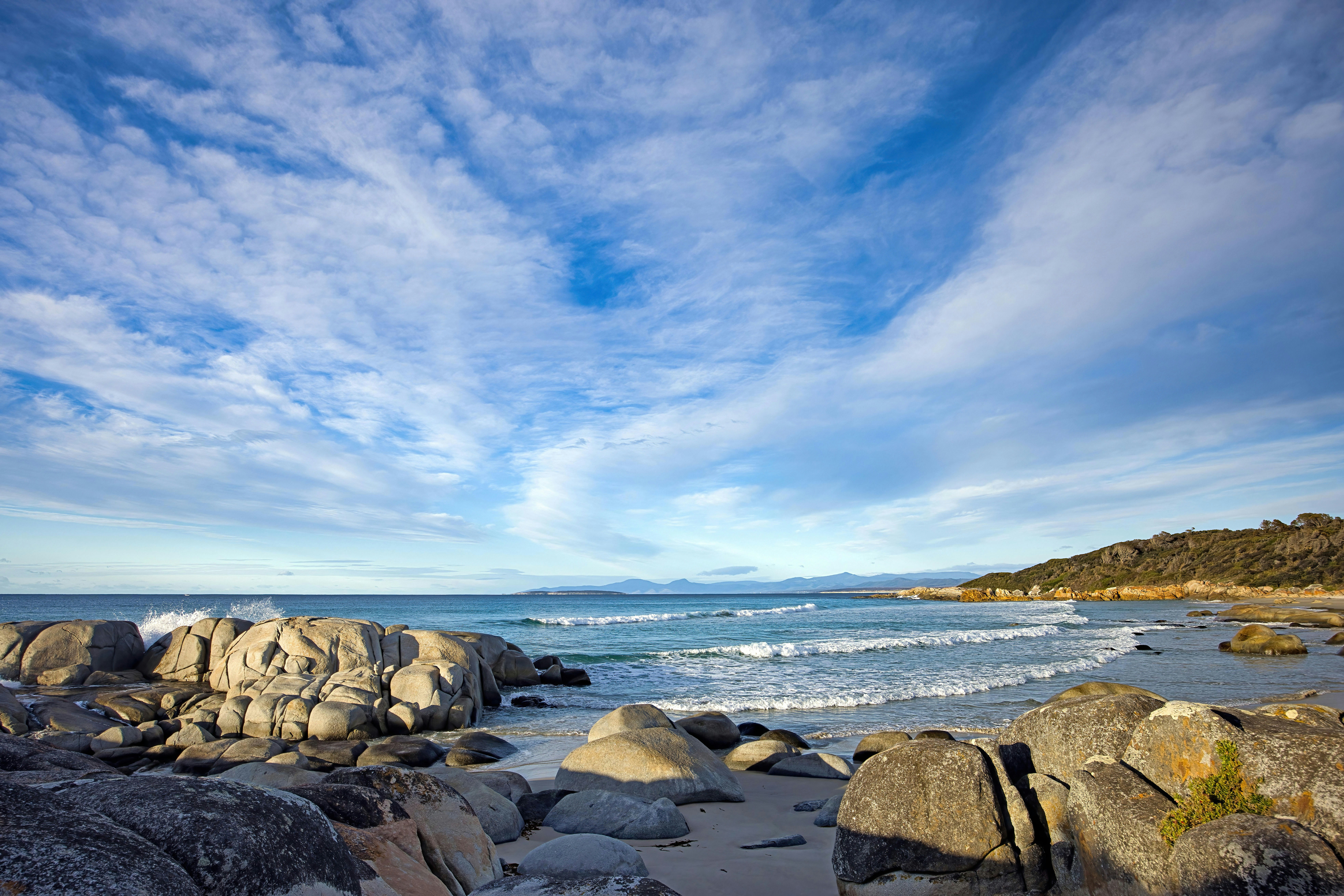 Rocky beach with waves under a cloudy blue sky