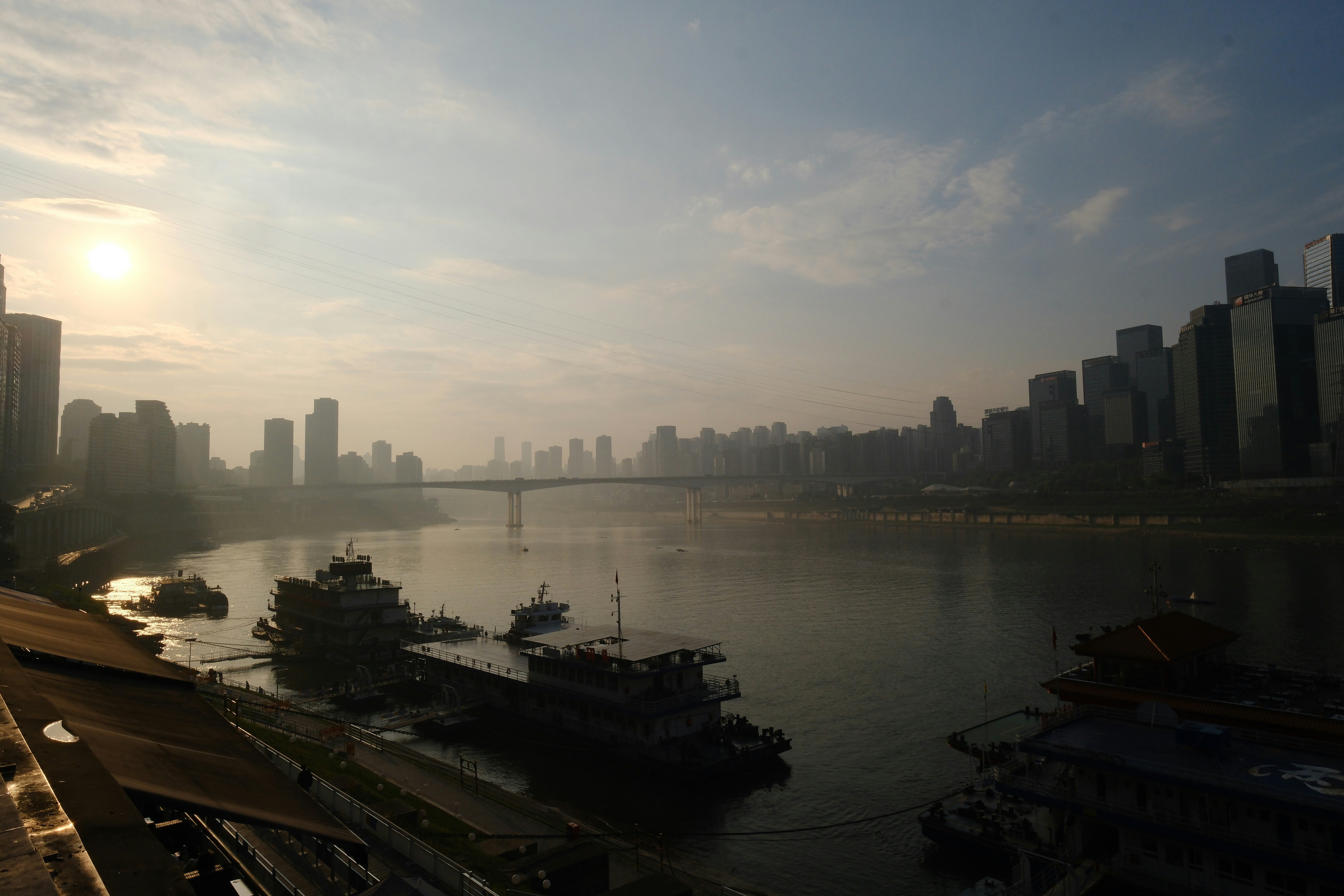 Sunrise over a foggy cityscape with boats on the river.