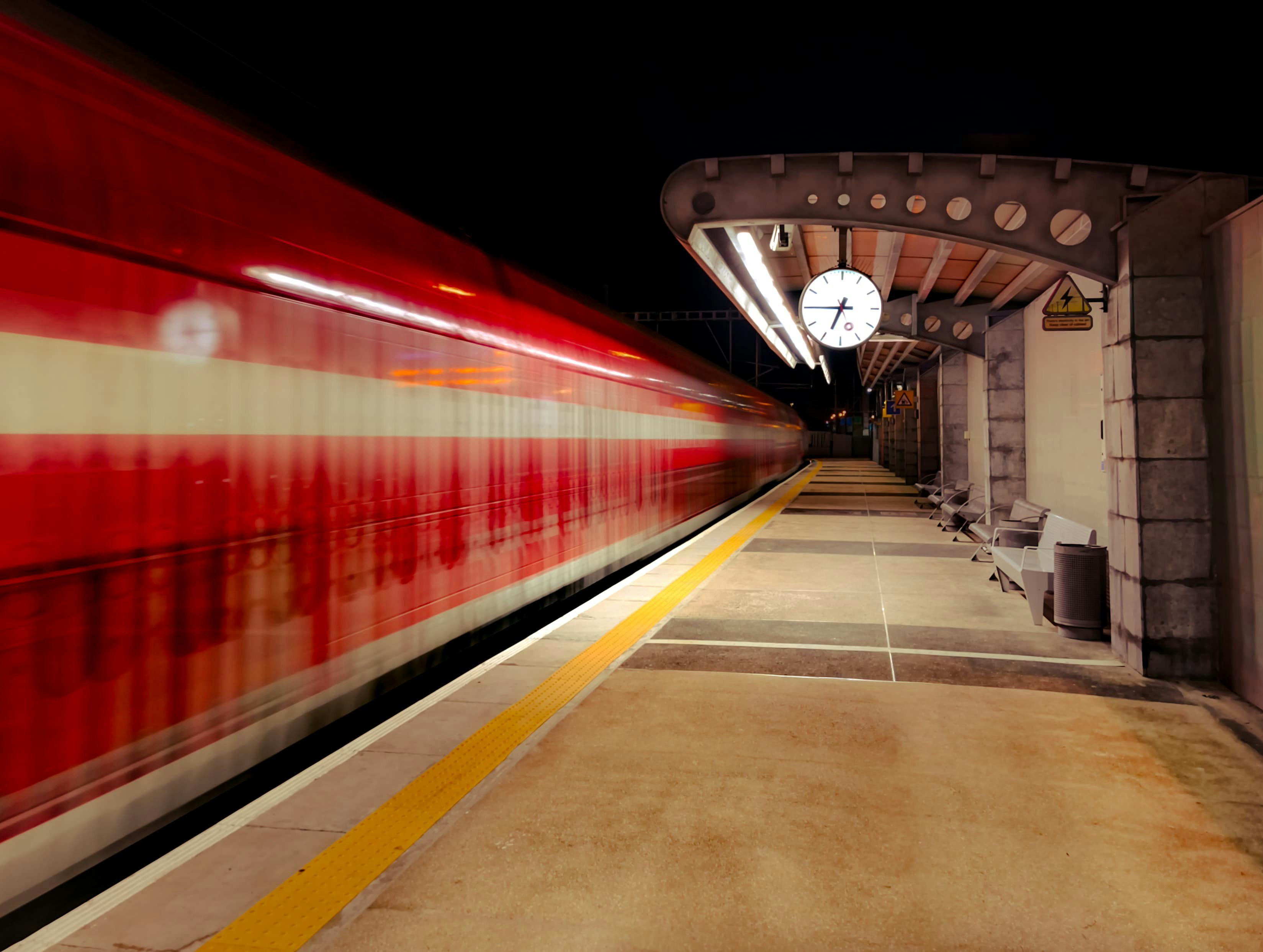 Red train blurring past a dark station