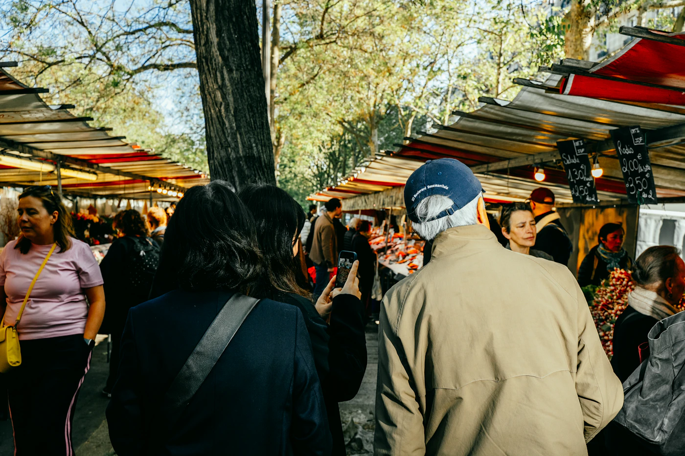 People browsing produce and flower stalls at a busy outdoor market