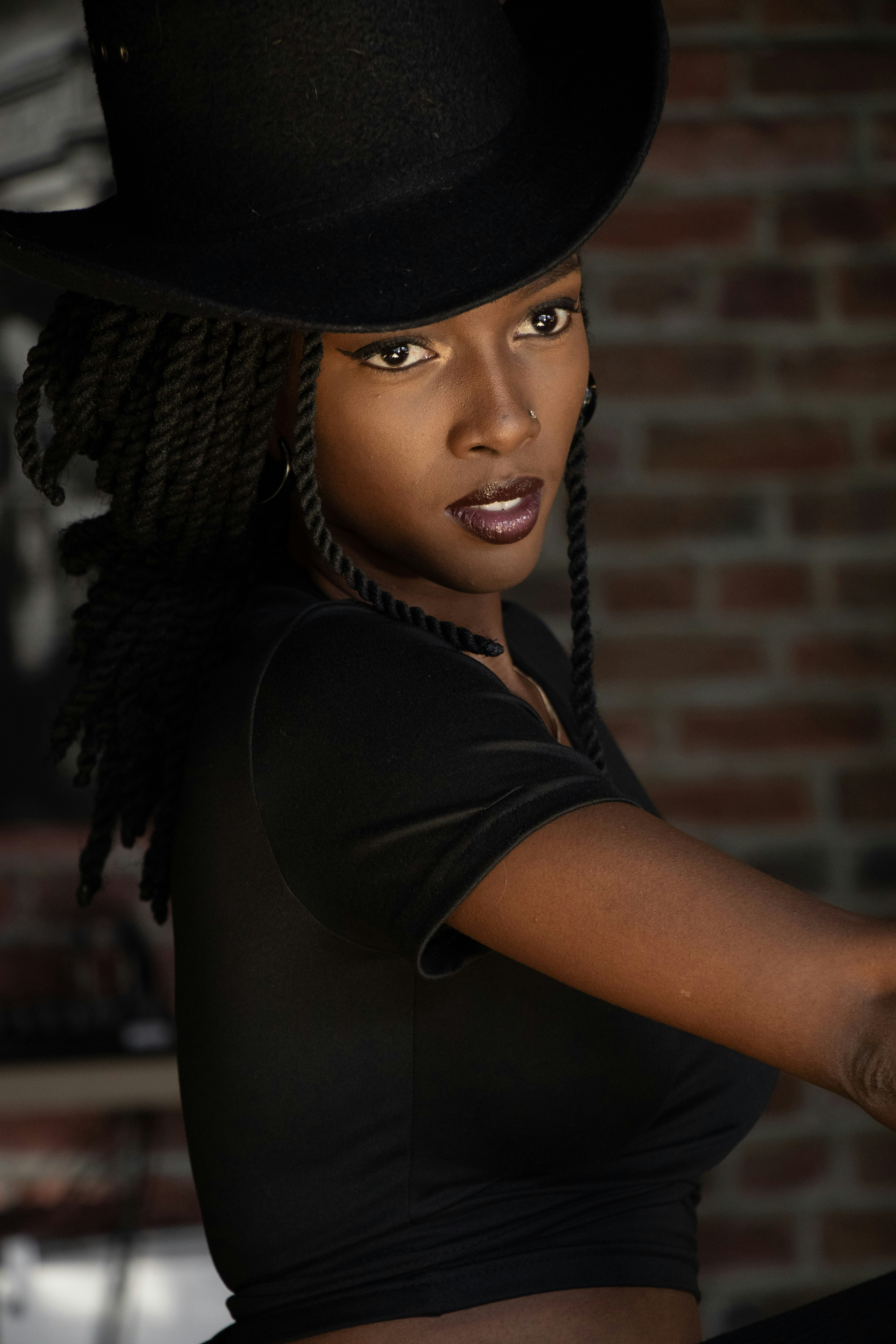 Woman in black hat and shirt with braided hair.
