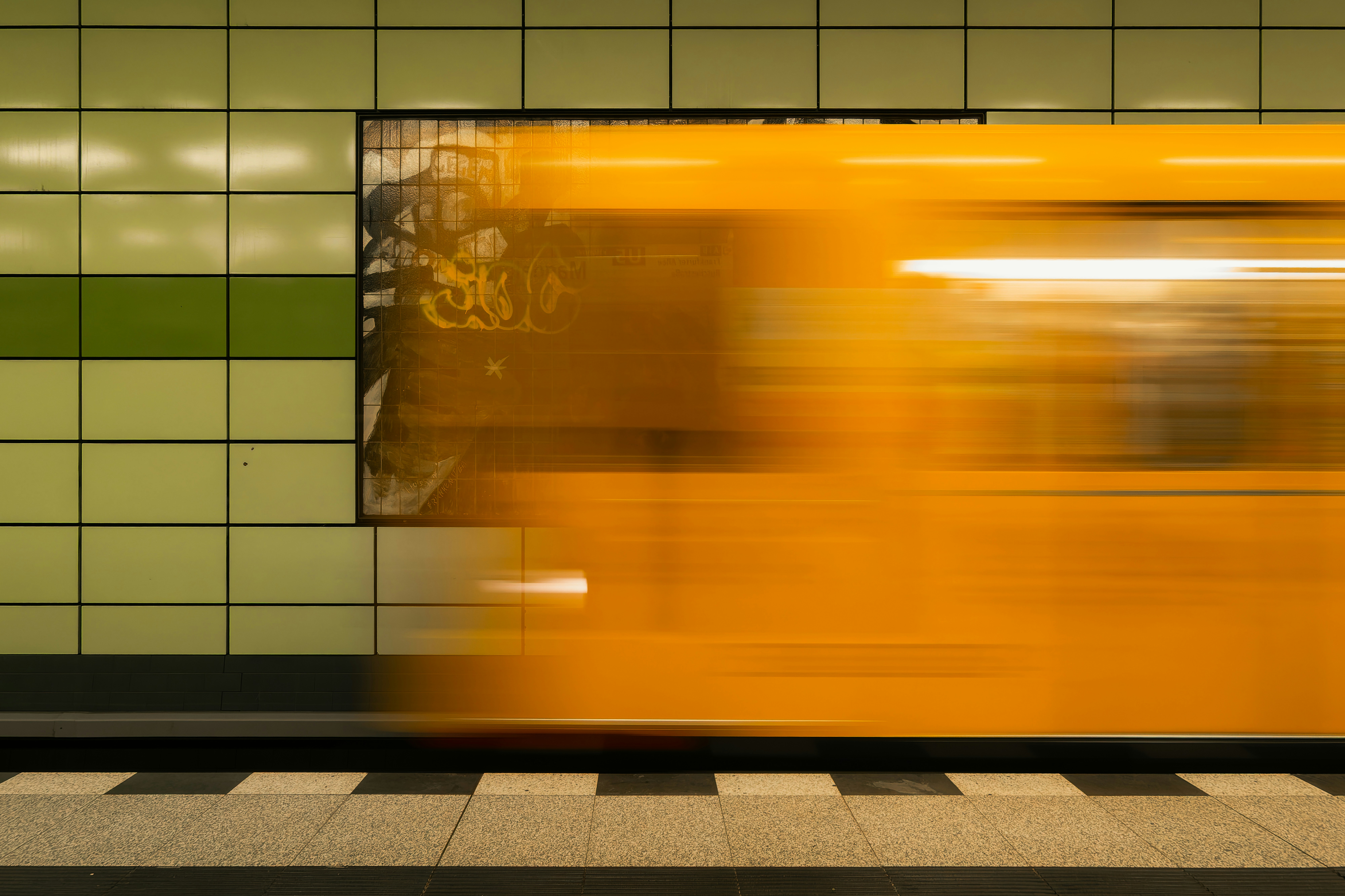 Yellow subway train blurred in motion at station.