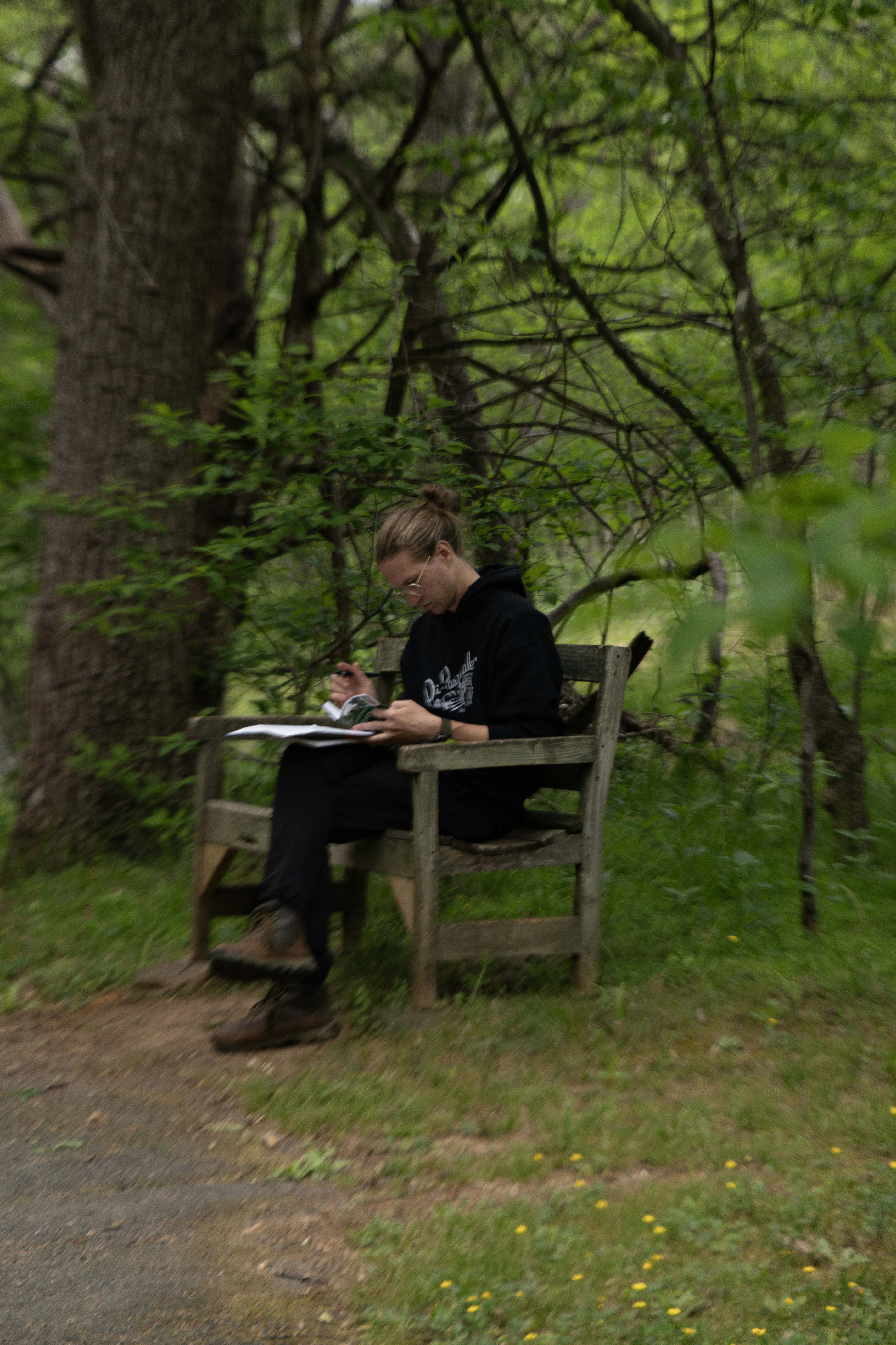 A person sketching on a wooden bench in a forest.
