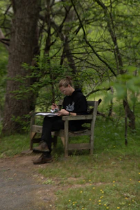 A person sketching on a wooden bench in a forest