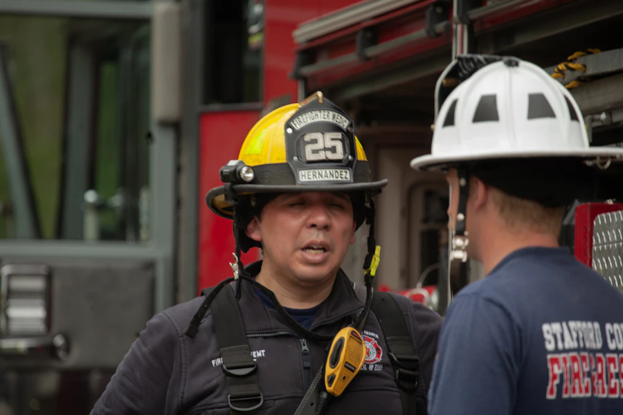 Two firefighters in helmets speaking beside a fire apparatus.