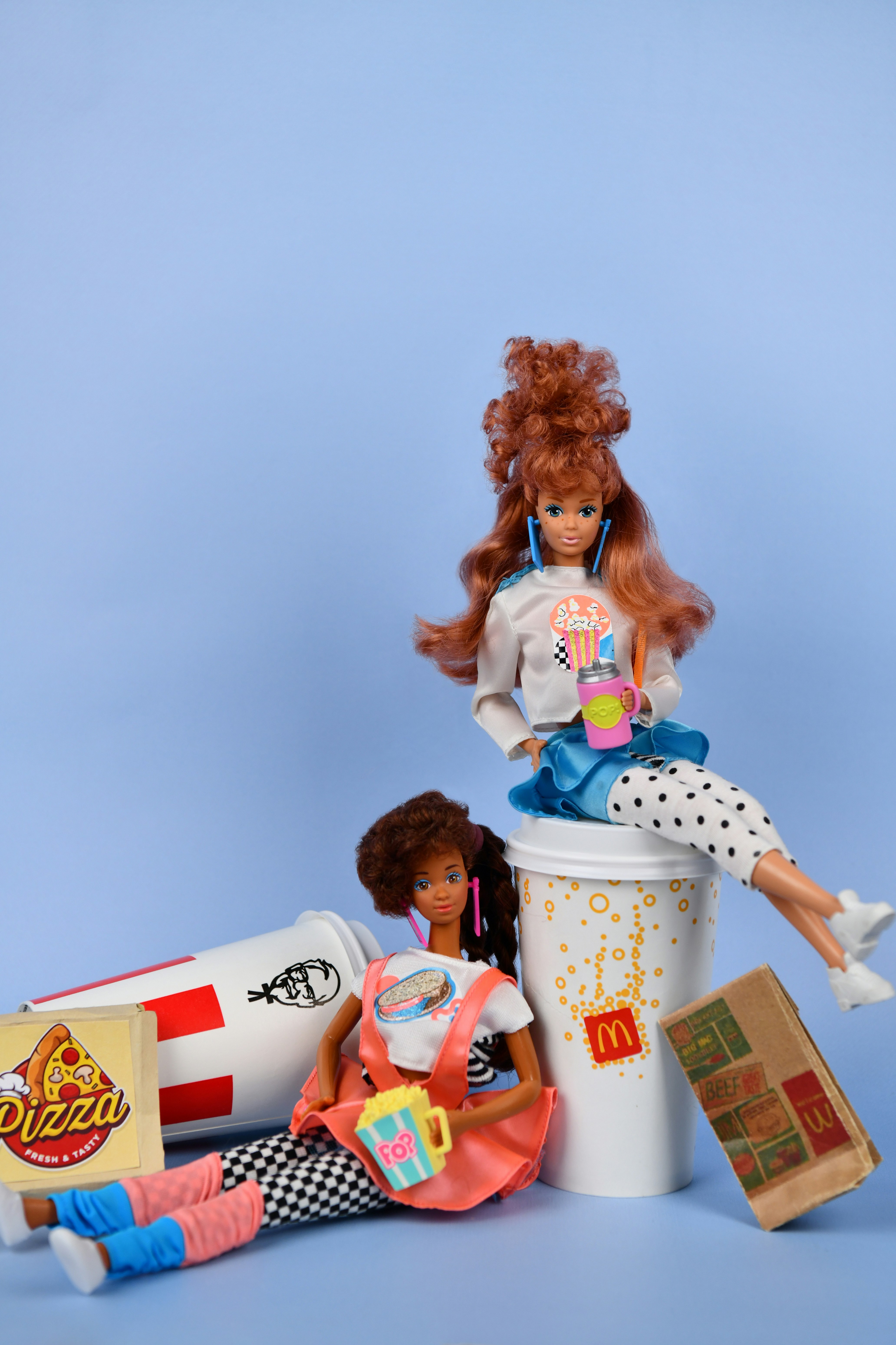 Two dolls with fast food and drinks on blue background