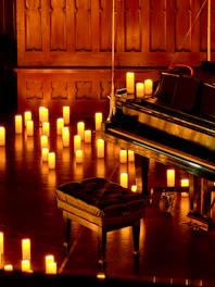 Grand piano and stool surrounded by glowing candles