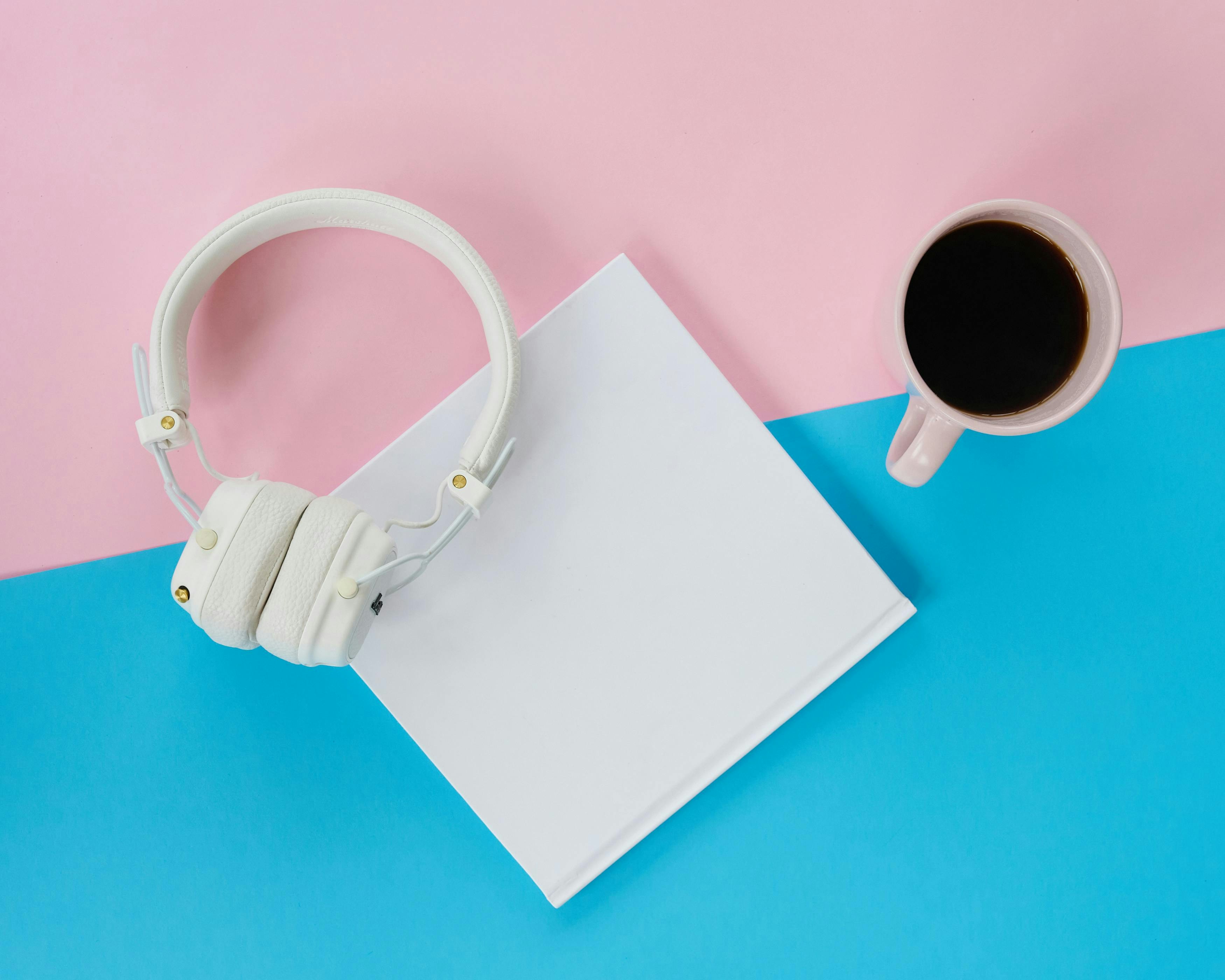 White headphones, blank book, and coffee on colorful background
