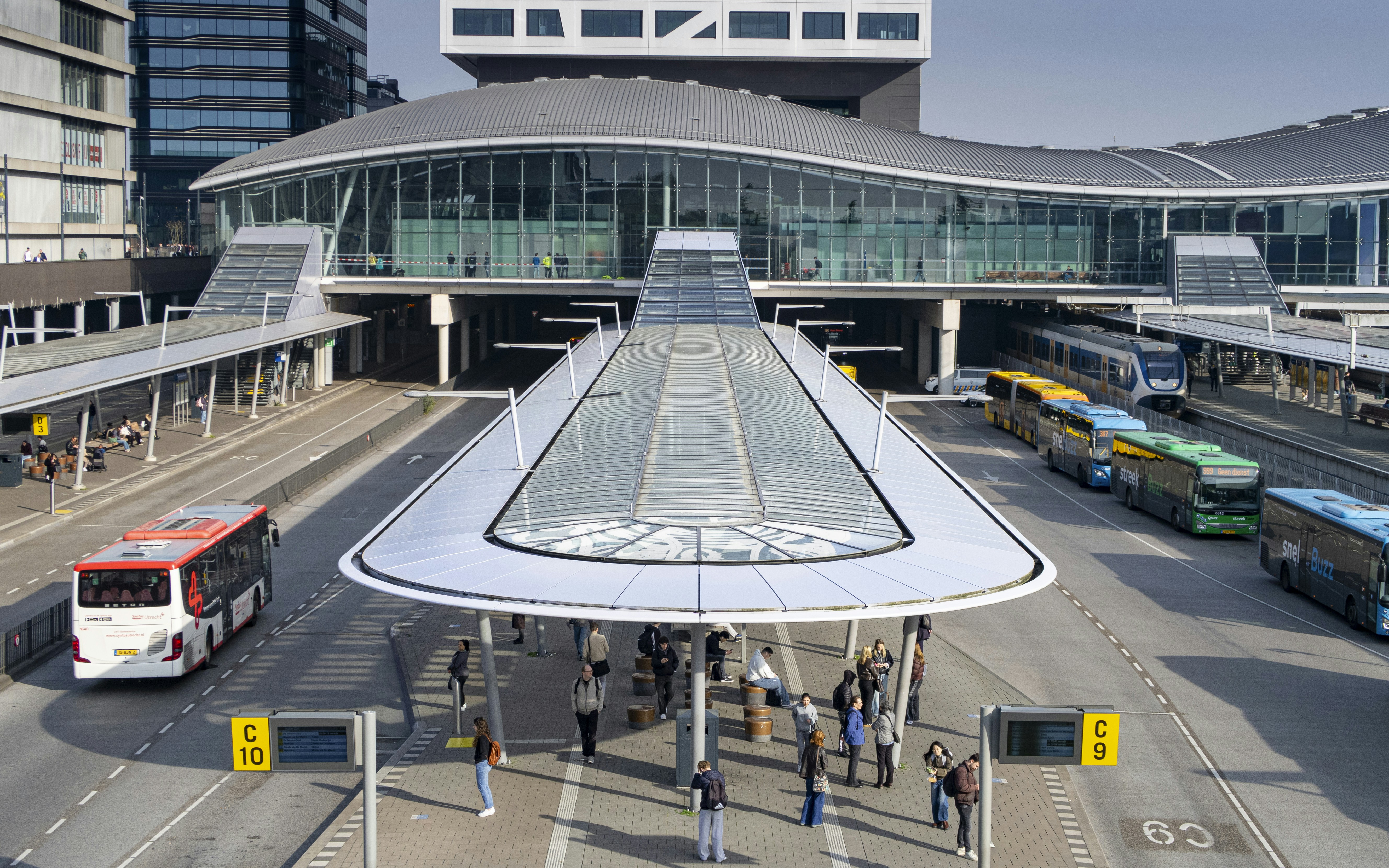 Modern bus station with multiple buses and people waiting.