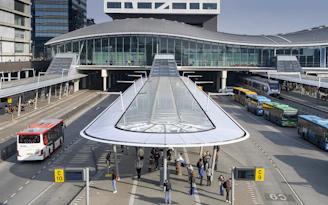 Modern bus station with multiple buses and people waiting.