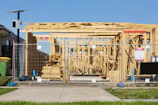 Wooden house frame under construction behind a fence.