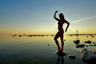 Woman posing on rocks by the ocean at sunset