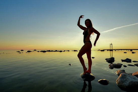 Woman posing on rocks by the ocean at sunset