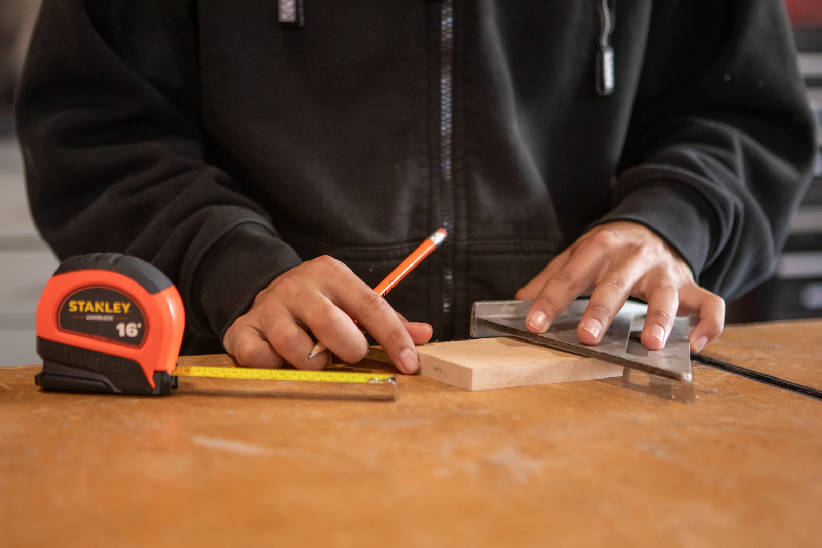 Hands measuring and marking wood with a pencil and metal square