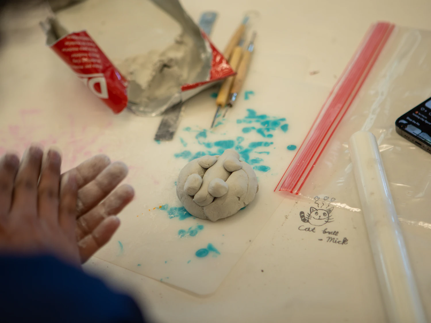 A child's hands shaping clay with small sculpting tools at a table