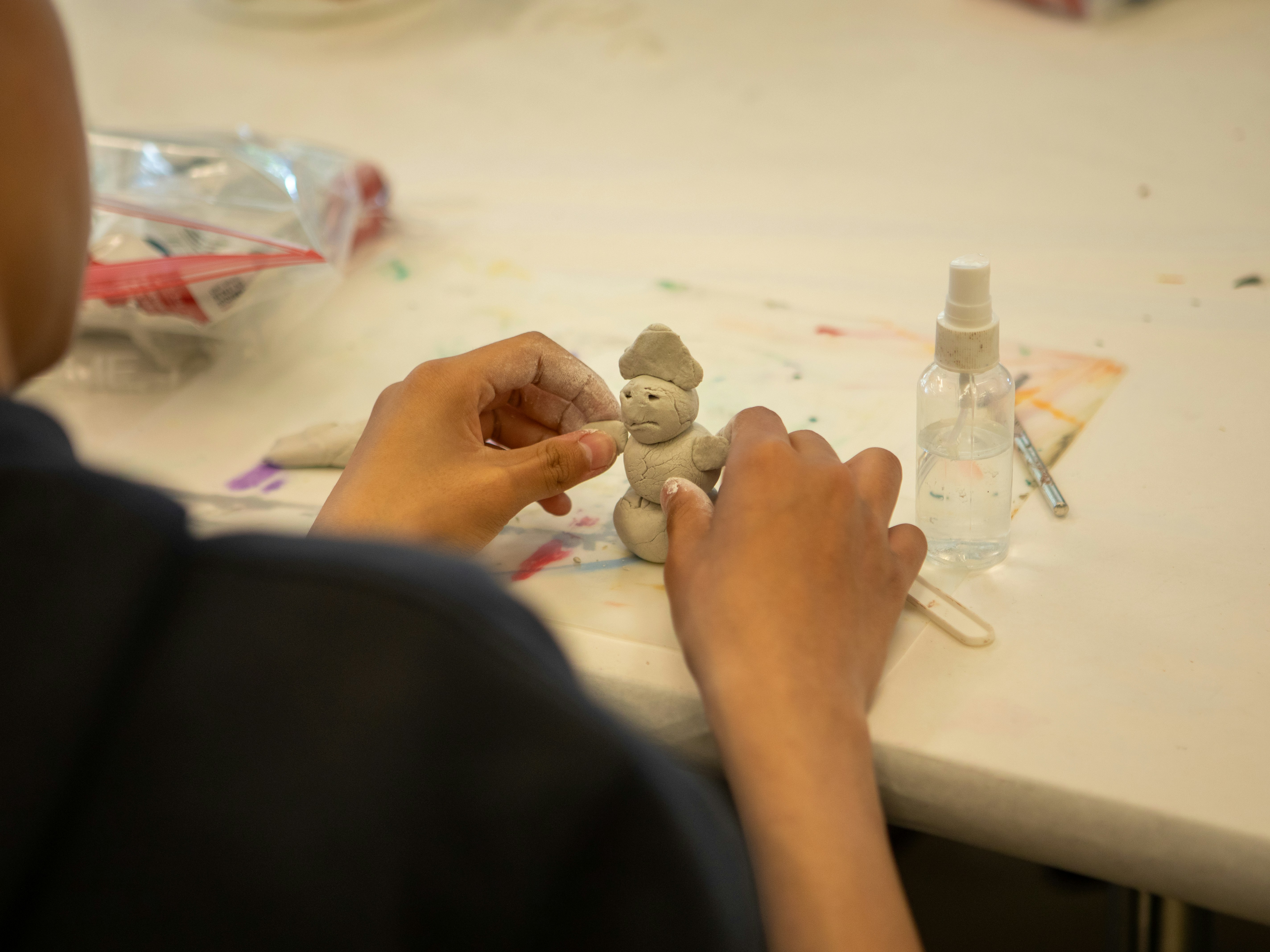 A child molds a small clay figure on a table.
