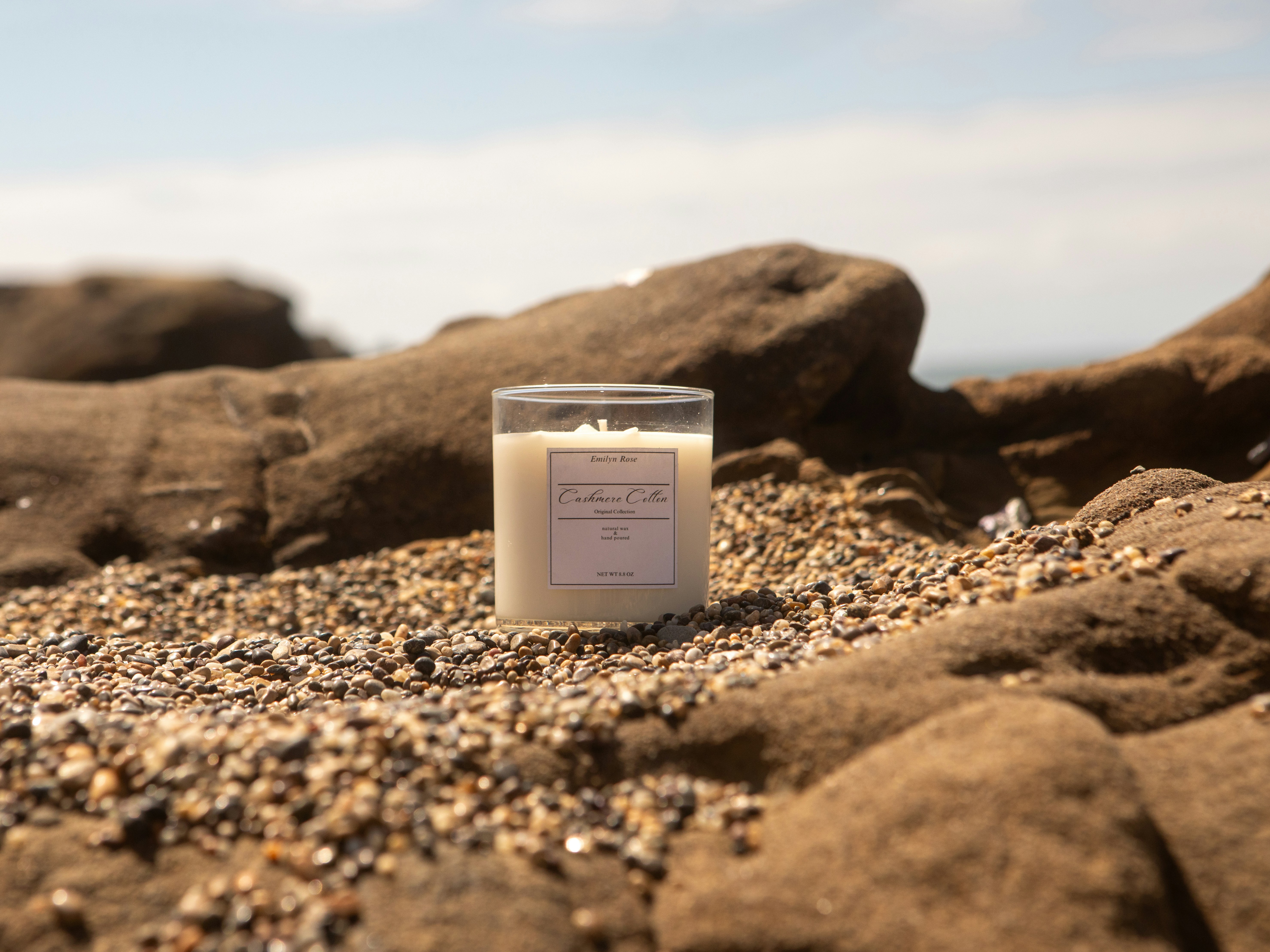 Candle sitting on a rocky beach with ocean background