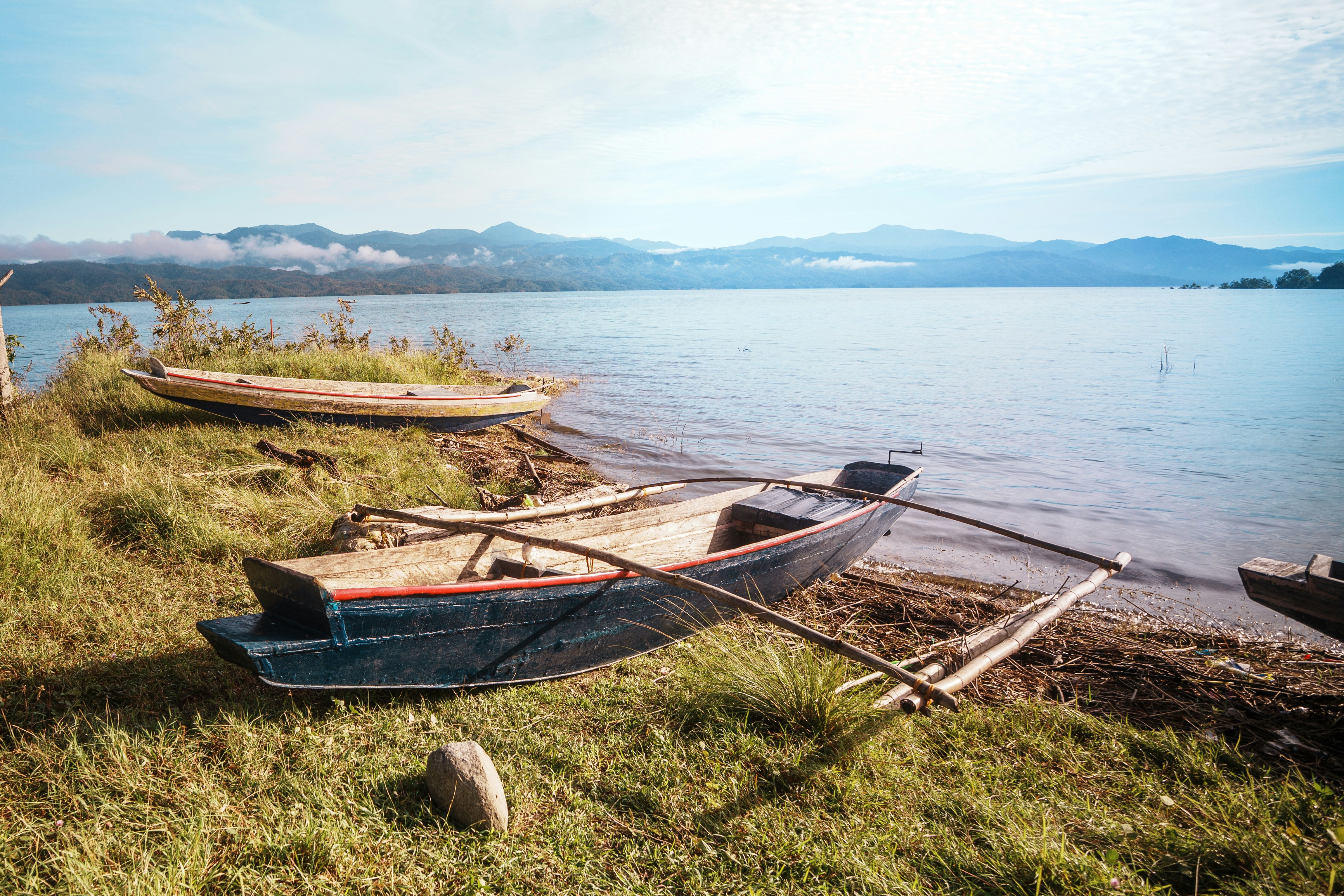 Traditional outrigger canoes rest on a grassy shore.