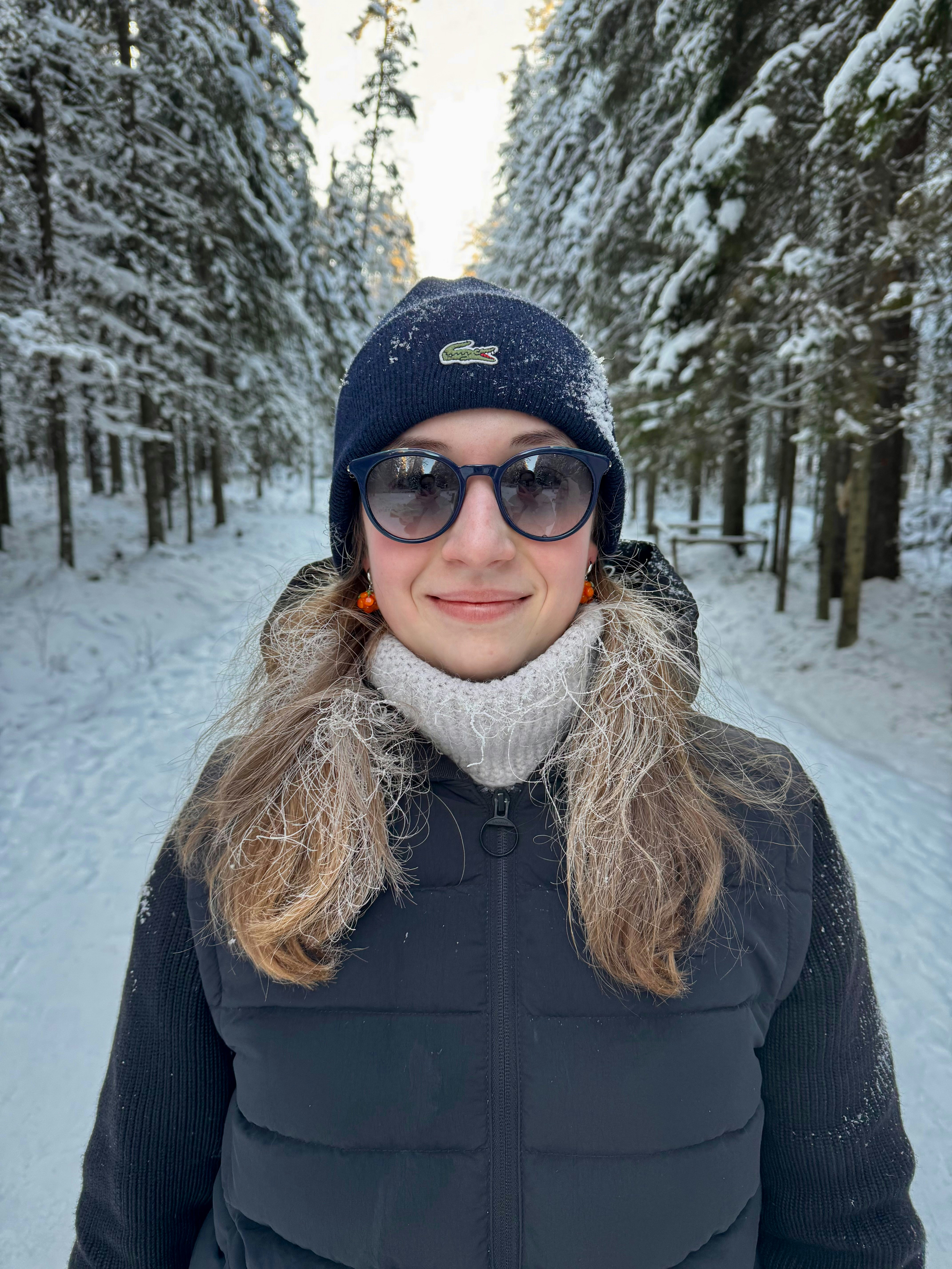 Woman in a snowy forest wearing a hat and sunglasses