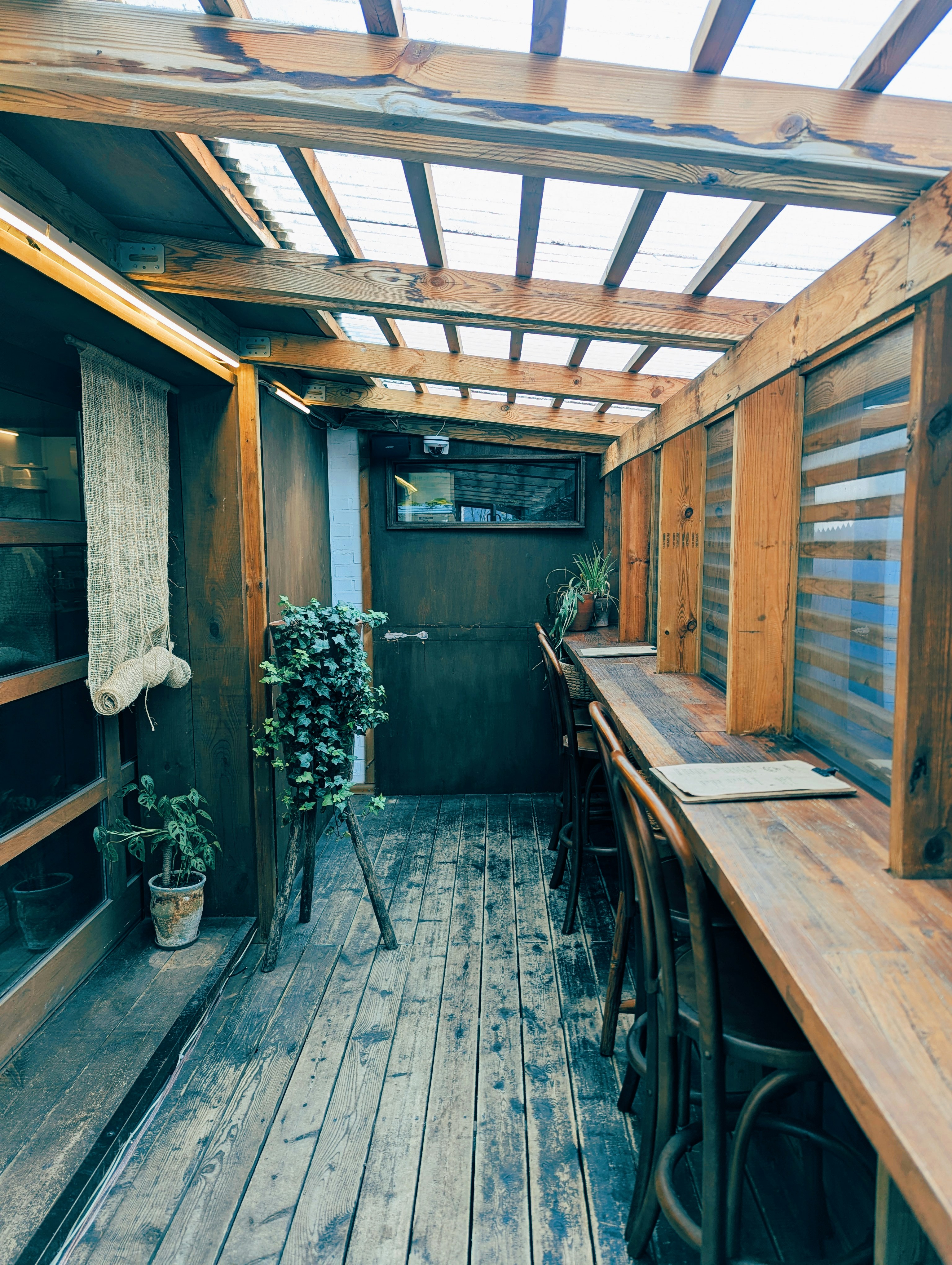 Area tempat duduk kafe outdoor kayu dengan tanaman