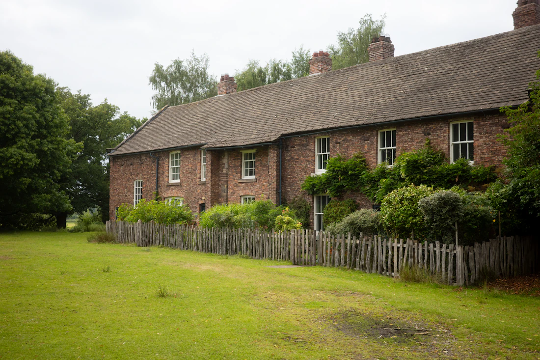 An old brick building behind a wooden fence and garden