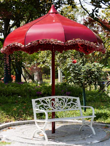 A white ornate bench sits beneath a red umbrella.