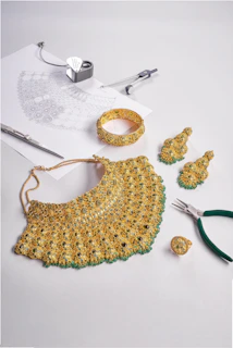 Gold jewelry set with green stones and design sketch.