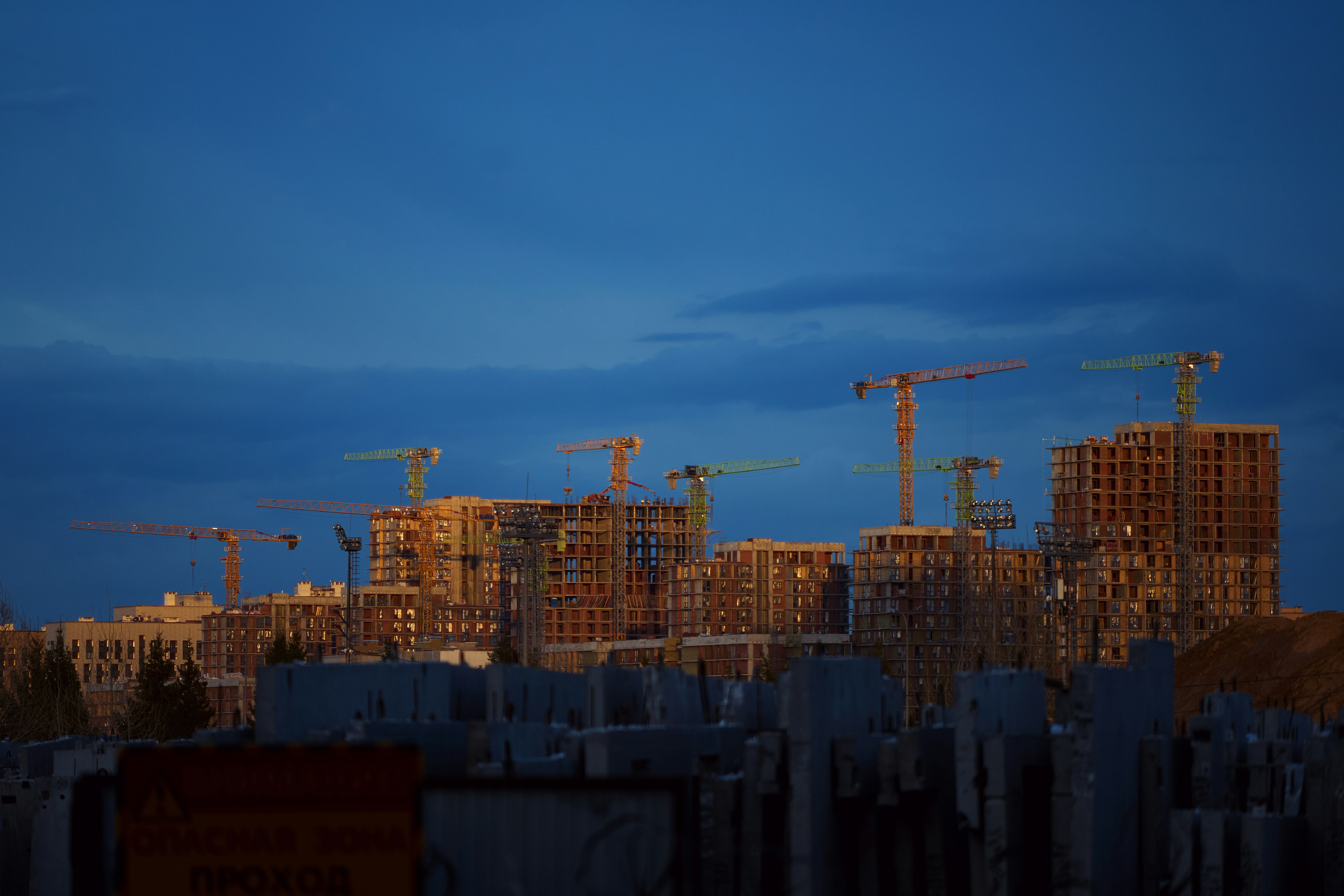 Construction cranes tower over unfinished buildings at dusk