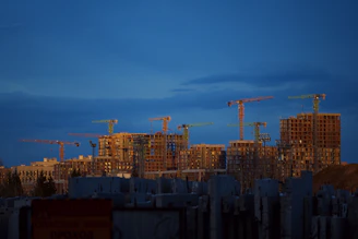 Construction cranes tower over unfinished buildings at dusk