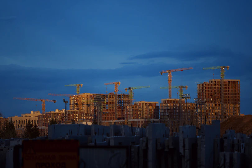 Construction cranes tower over unfinished buildings at dusk