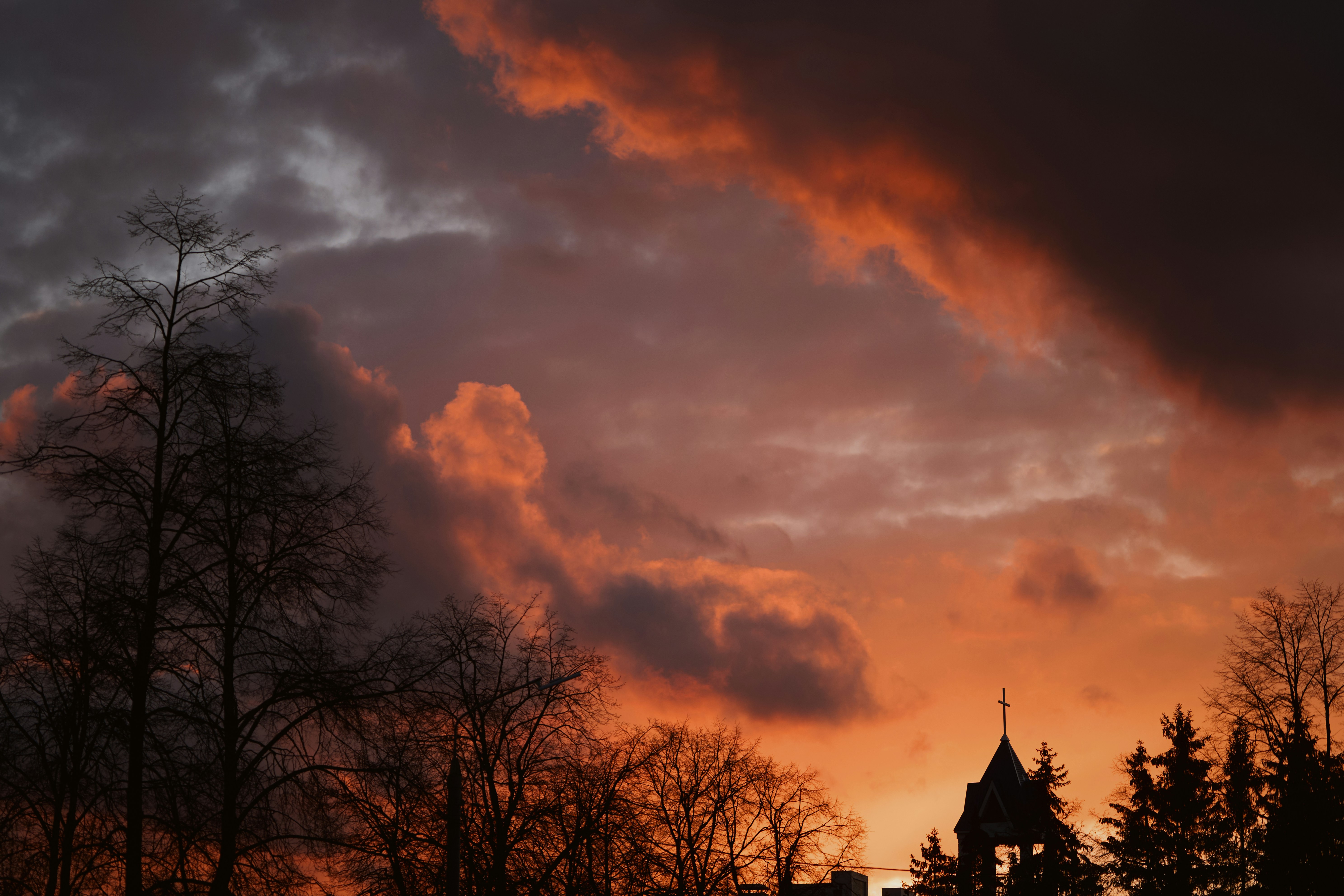 Dramatic sunset sky with silhouetted trees and a steeple.