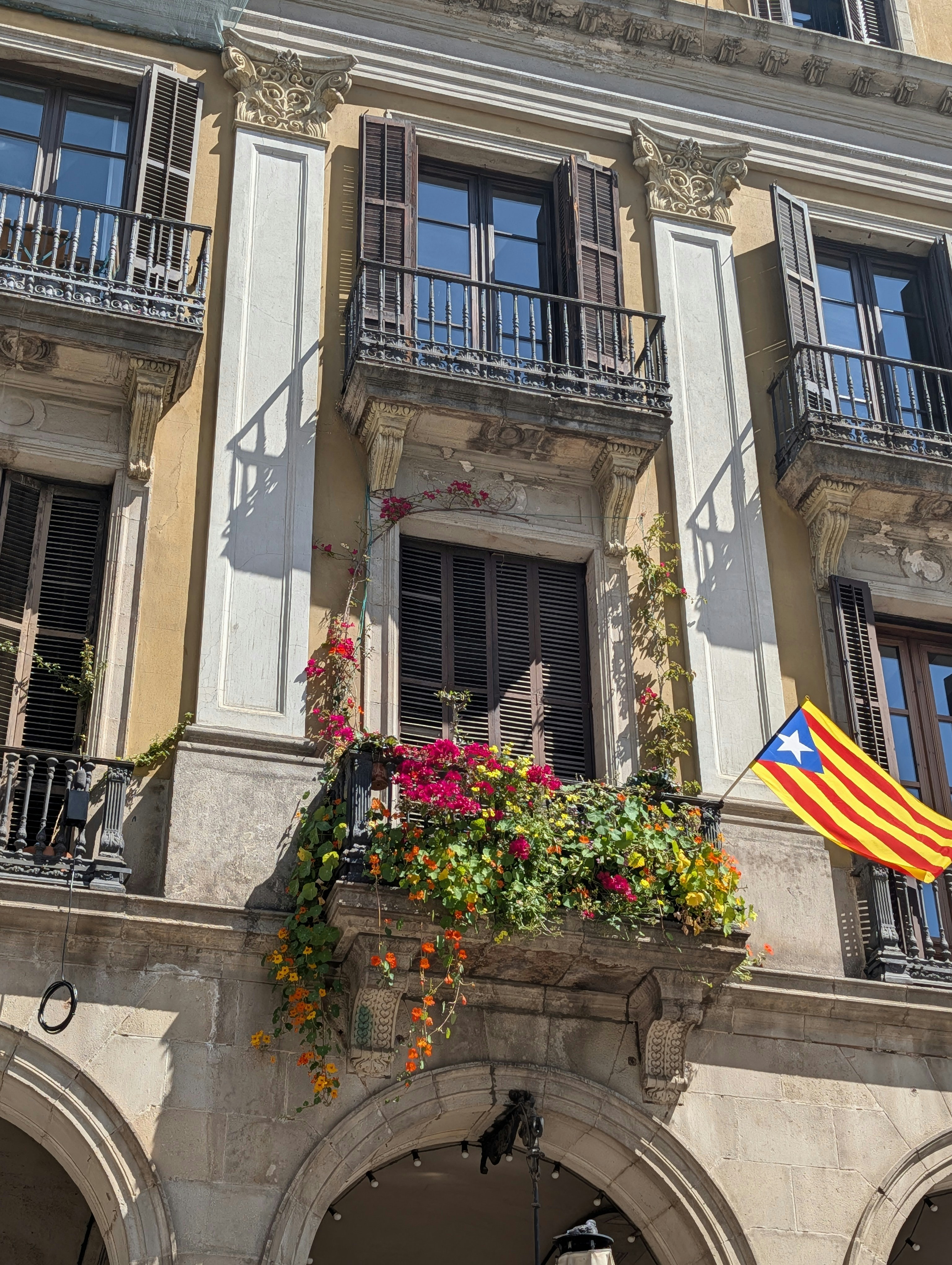 Balcony overflowing with colorful flowers and a catalan flag.