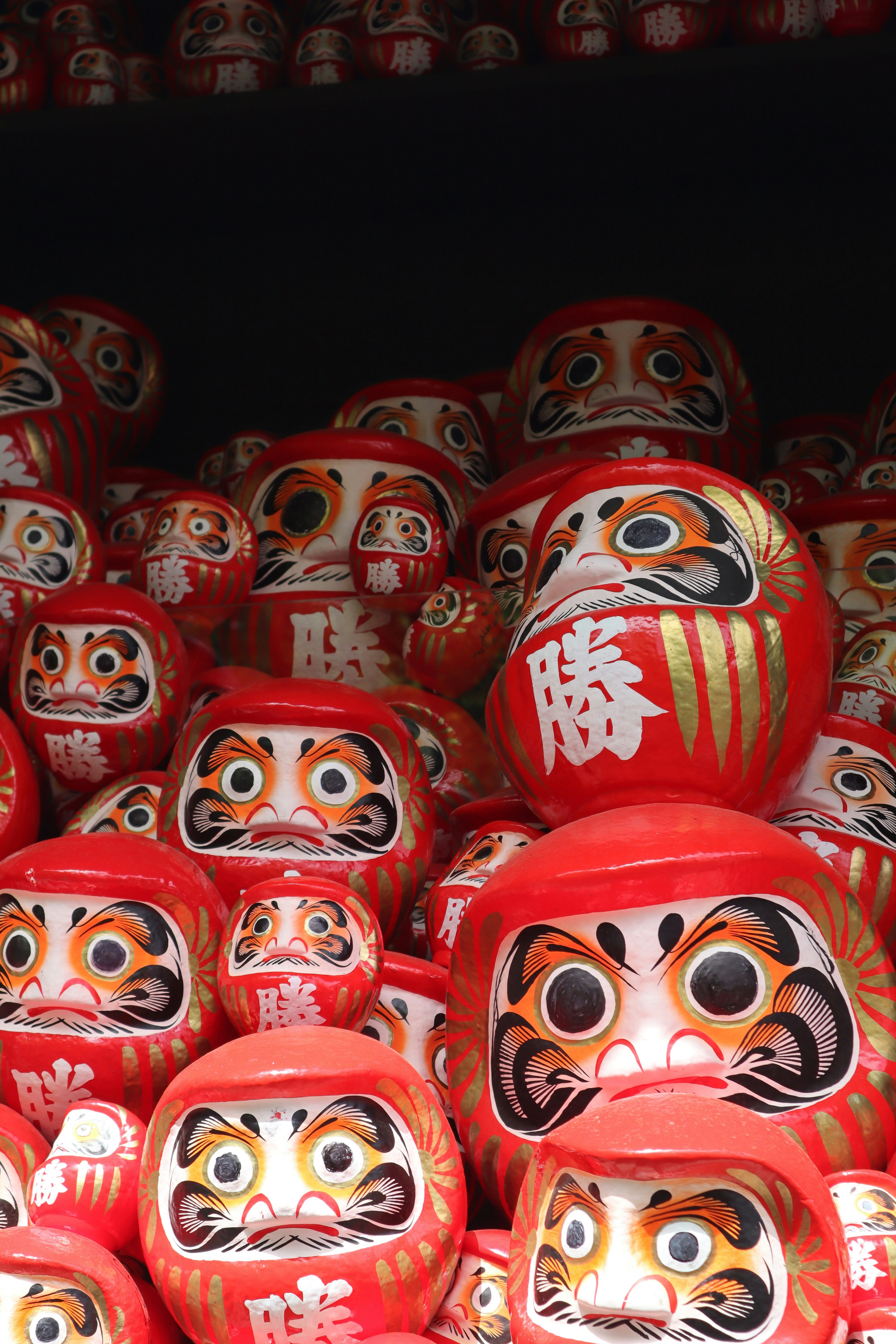 Una colección de muñecos daruma rojos con caras pintadas.